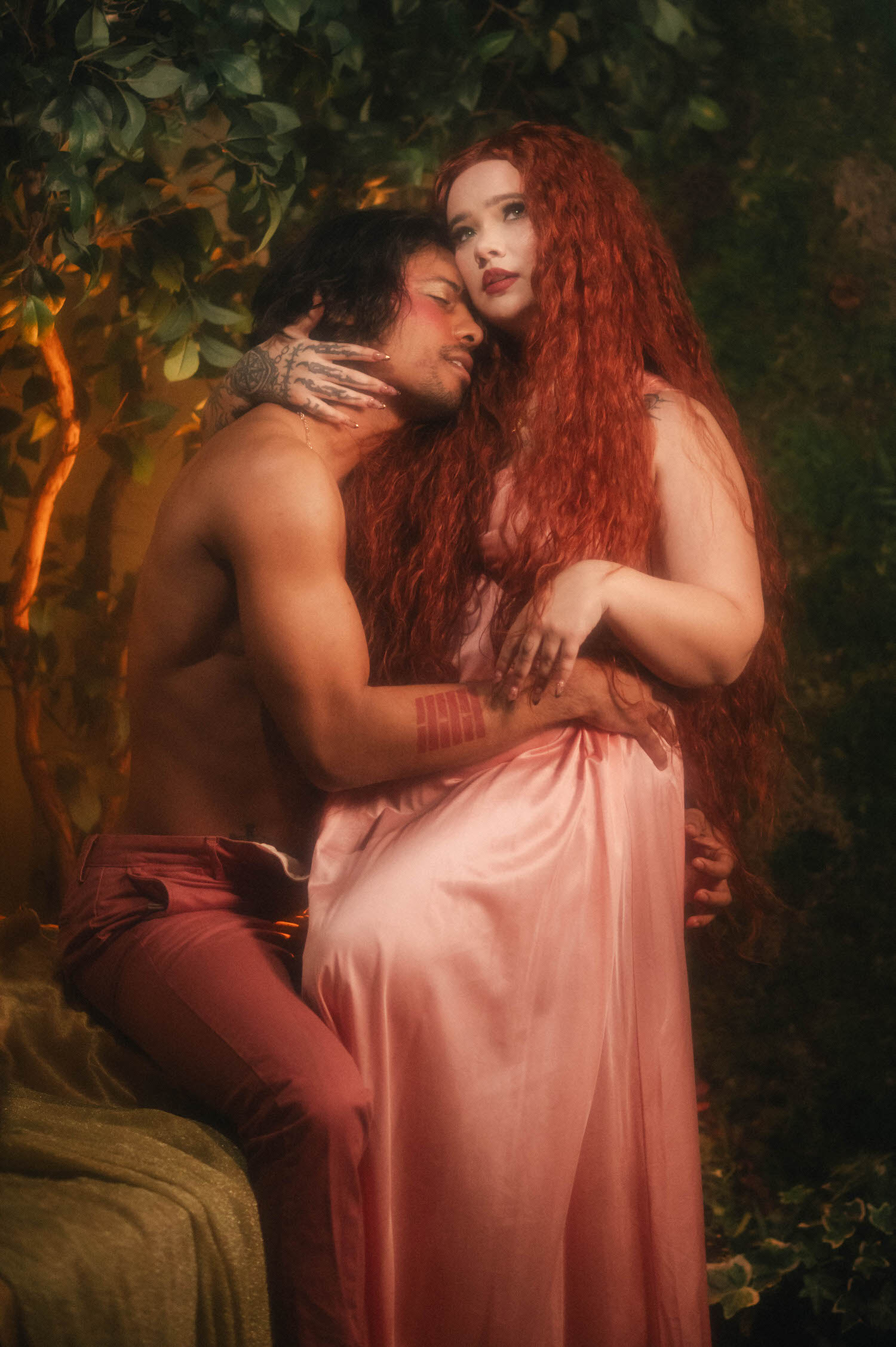Intimate portrait of a couple embracing outdoors, the woman's wine red lips and vintage waves evoking classical portraiture while her partner holds her waist beneath draped pink silk. Royal Lune Photo