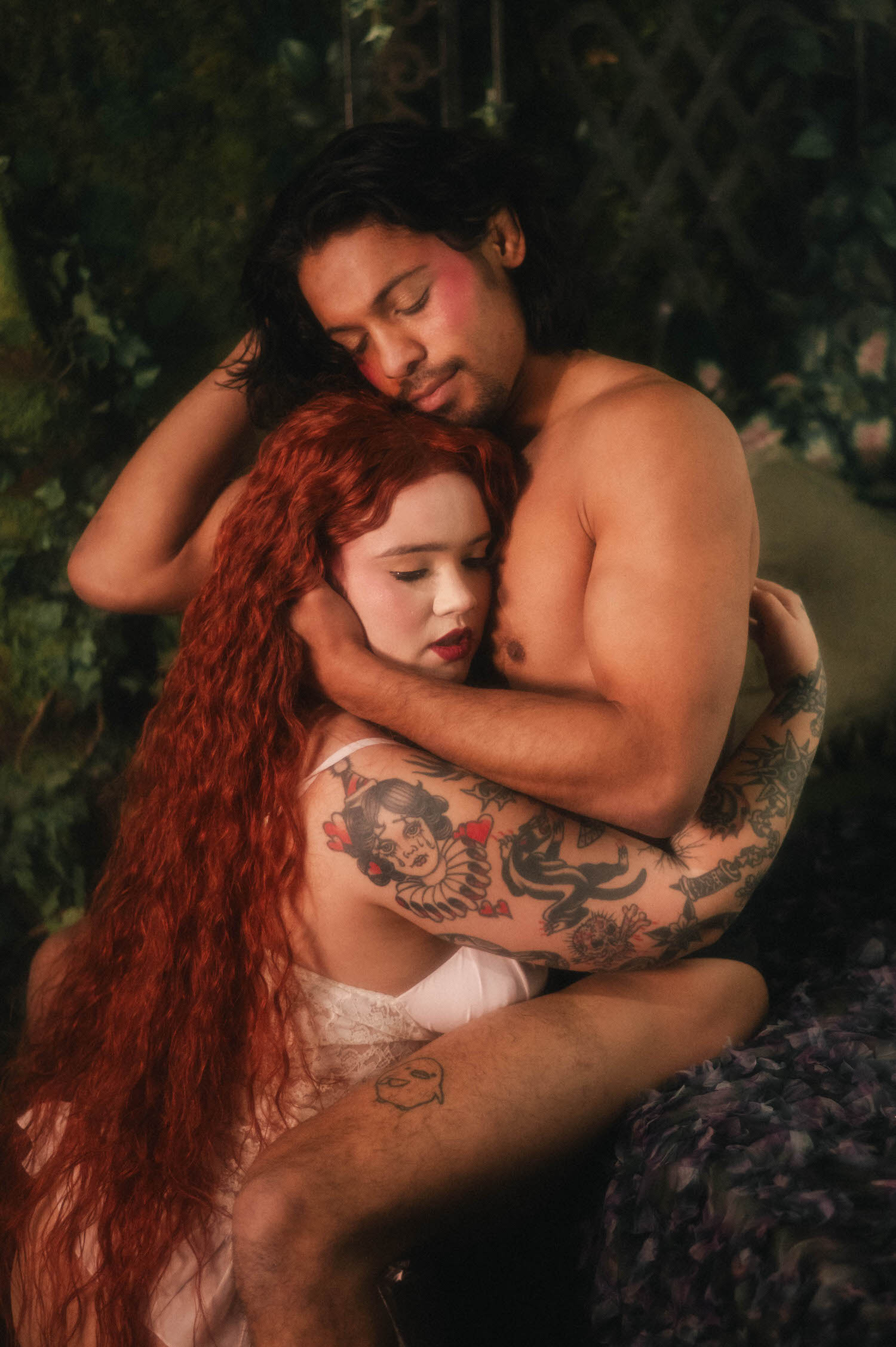Couples boudoir photoshoot ideas captured in an intimate embrace, the woman's tattooed shoulder pressed close as her partner holds her waist against an iron and lace backdrop. Royal Lune Photo