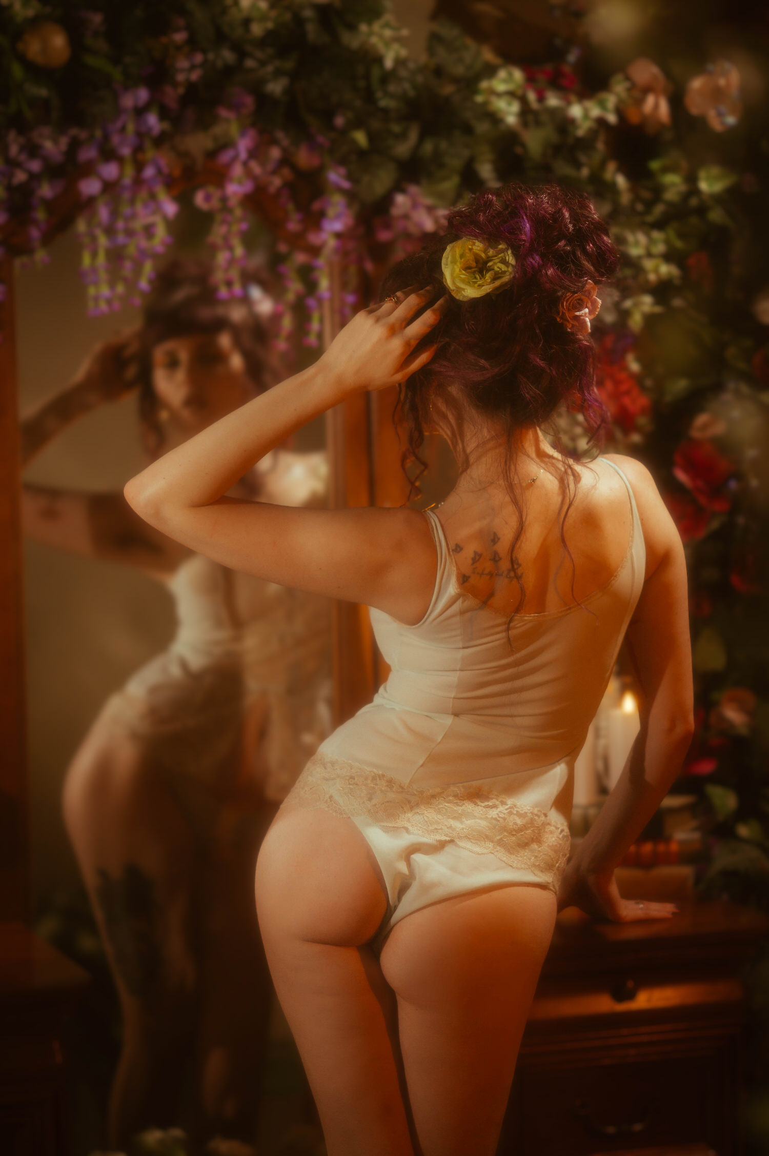 A model tilts her head back against a wooden dresser in a vintage mint green lingerie set by Vanity Fair with rose straps, surrounded by red roses and a lit candle, captured in a dark fairytale boudoir photoshoot at Royal Lune Photo.
