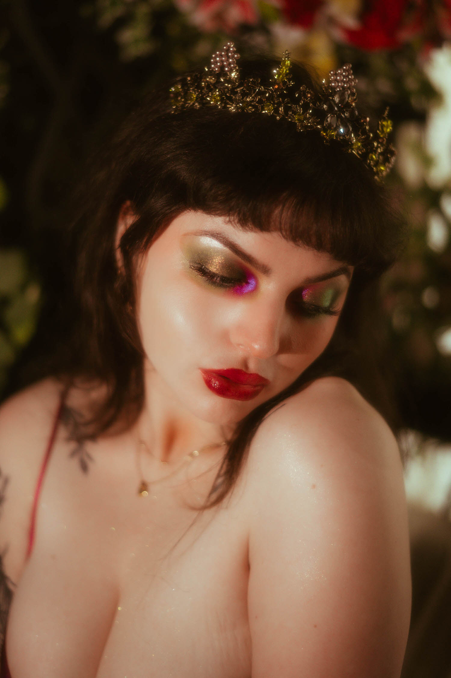 A close up portrait captures a bride's shimmering gold and pink eyeshadow, bold red lipstick, and jeweled tiara as she looks down softly during a moody boudoir lighting portrait at Royal Lune Studio, Royal Lune Photo.