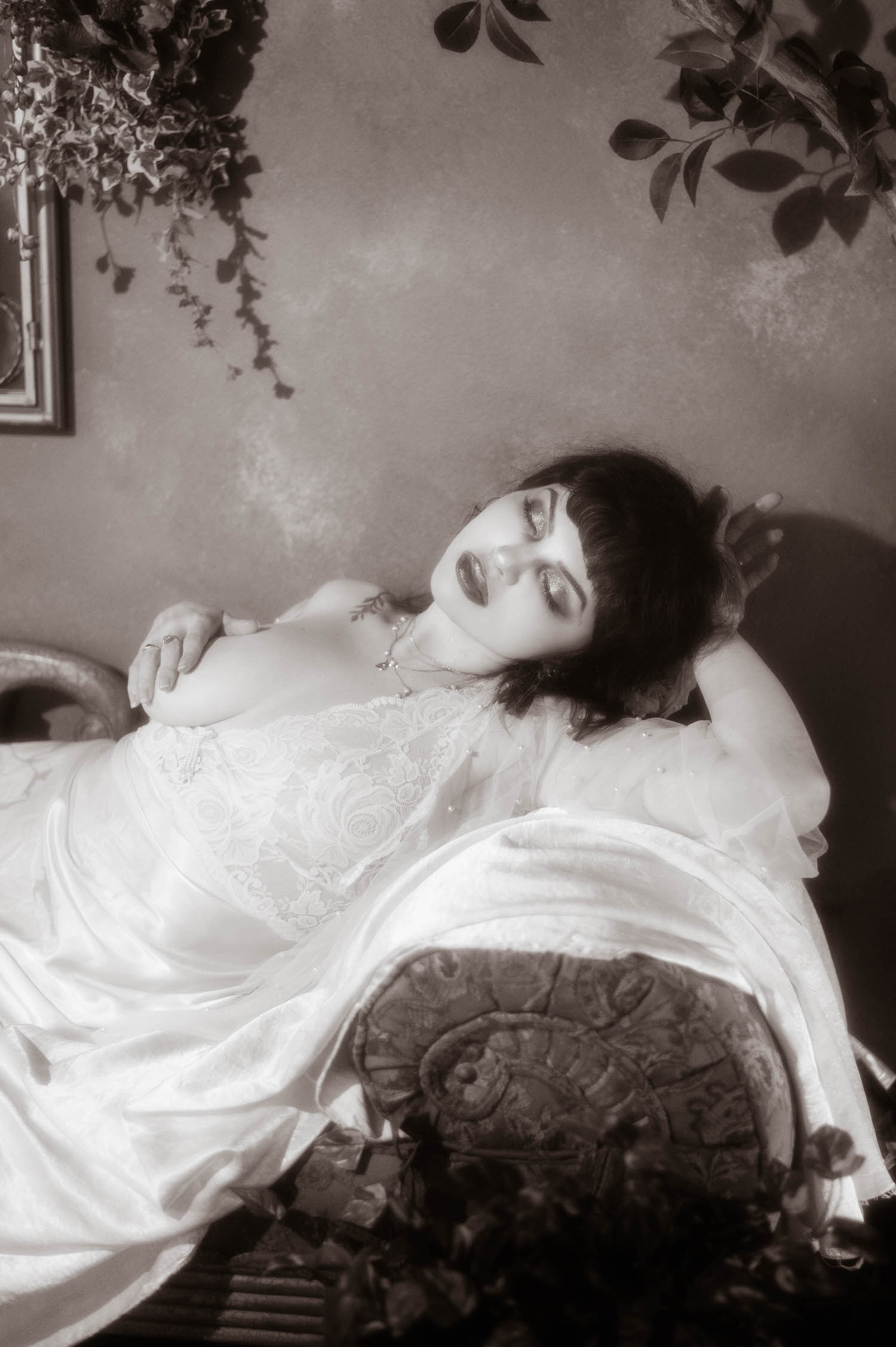 A black and white portrait shows a bride lying back with her eyes closed and one hand resting on her shoulder, soft highlights tracing her lace nightgown and pearl beaded sleeve at Royal Lune's vintage photo studio, Royal Lune Photo.