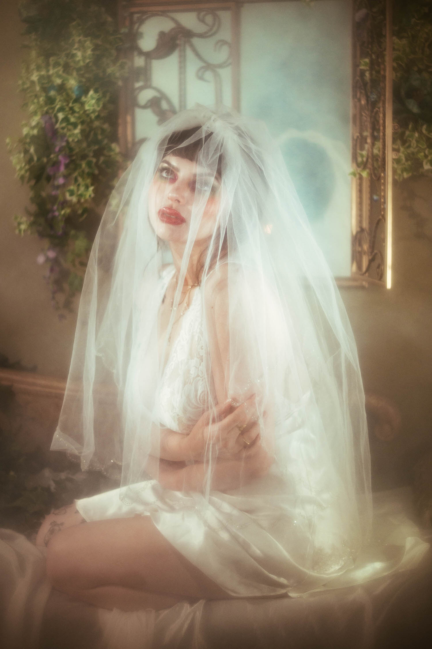 A bride sits with a full tulle veil draped over her lace nightgown and arms crossed at her chest, a teal tinted mirror glowing softly behind her during this moody boudoir lighting portrait at Royal Lune Studio, Royal Lune Photo.