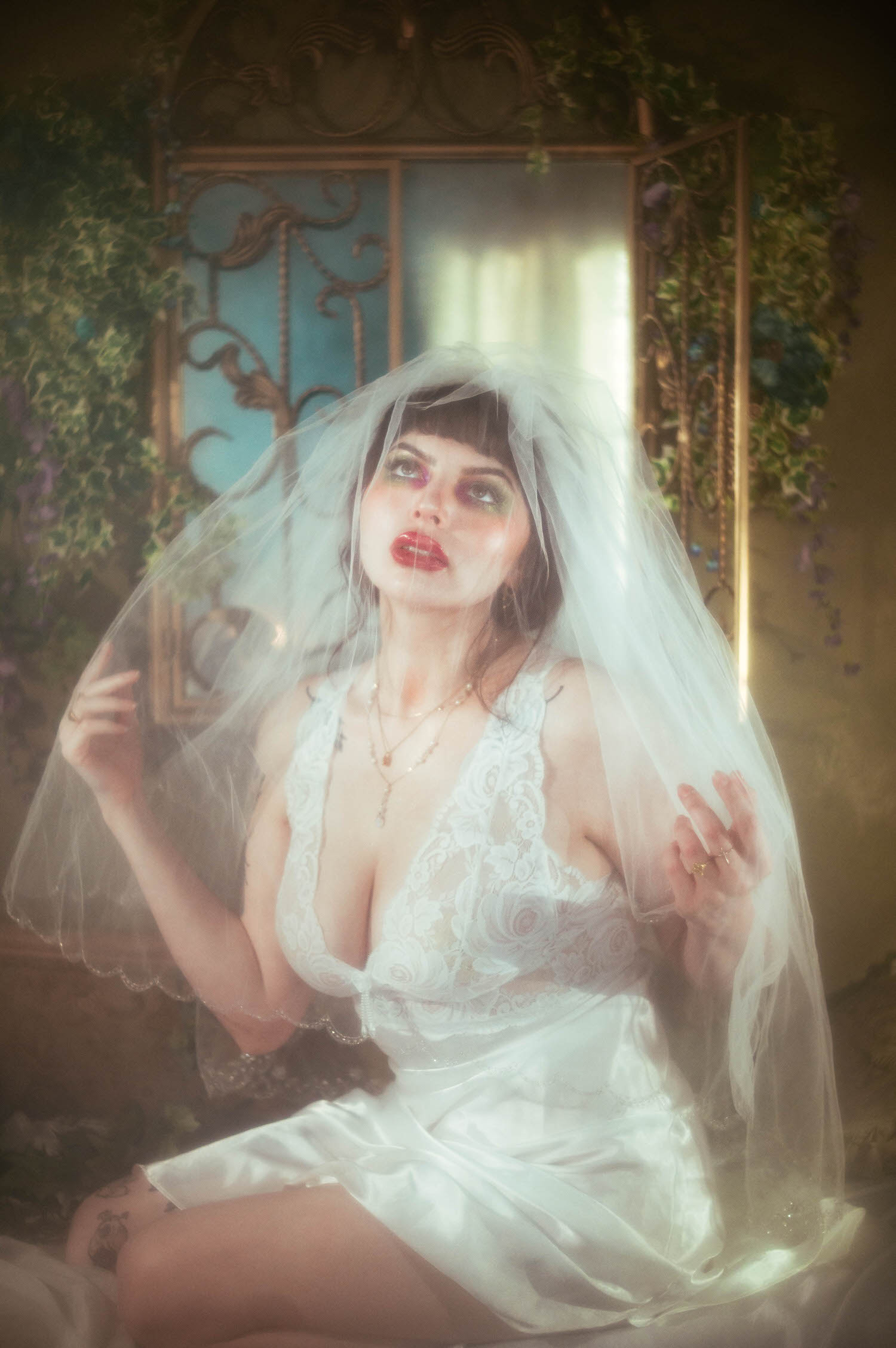 A bride tilts her head back beneath a sheer veil, her gaze lifted upward as bright window light glows through a teal mirror behind her during this bridal boudoir photography session at Royal Lune Studio, Royal Lune Photo.