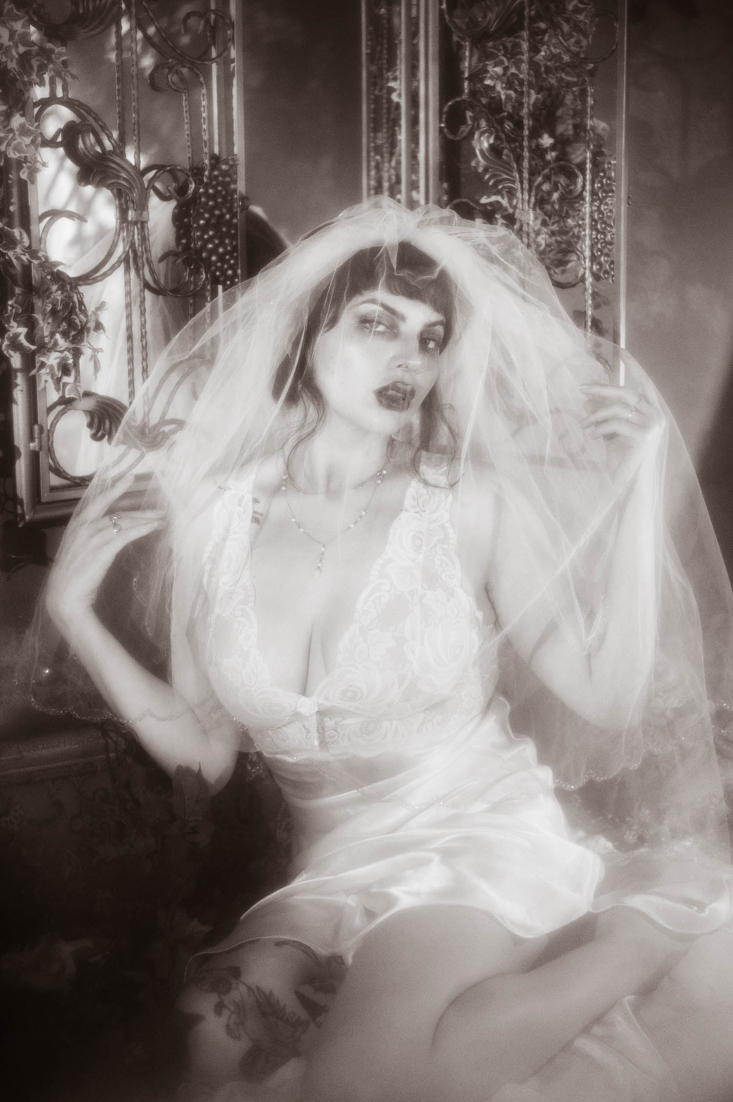 A black and white portrait shows a bride with one hand on her hip and her veil draped loosely as she gazes to the side, soft tonal contrast shaping this bridal boudoir photography image at Royal Lune Studio, Royal Lune Photo.