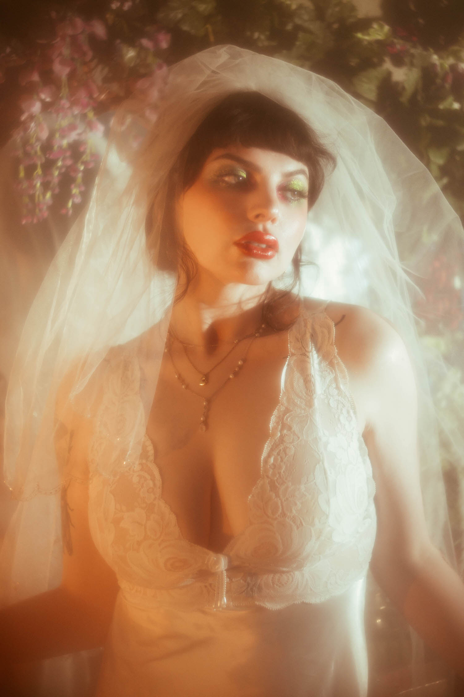 A close up portrait shows a bride's veil framing her face and shimmering green eyeshadow, warm golden light glowing across her lace nightgown bodice during this bridal boudoir photography session at Royal Lune Studio, Royal Lune Photo.