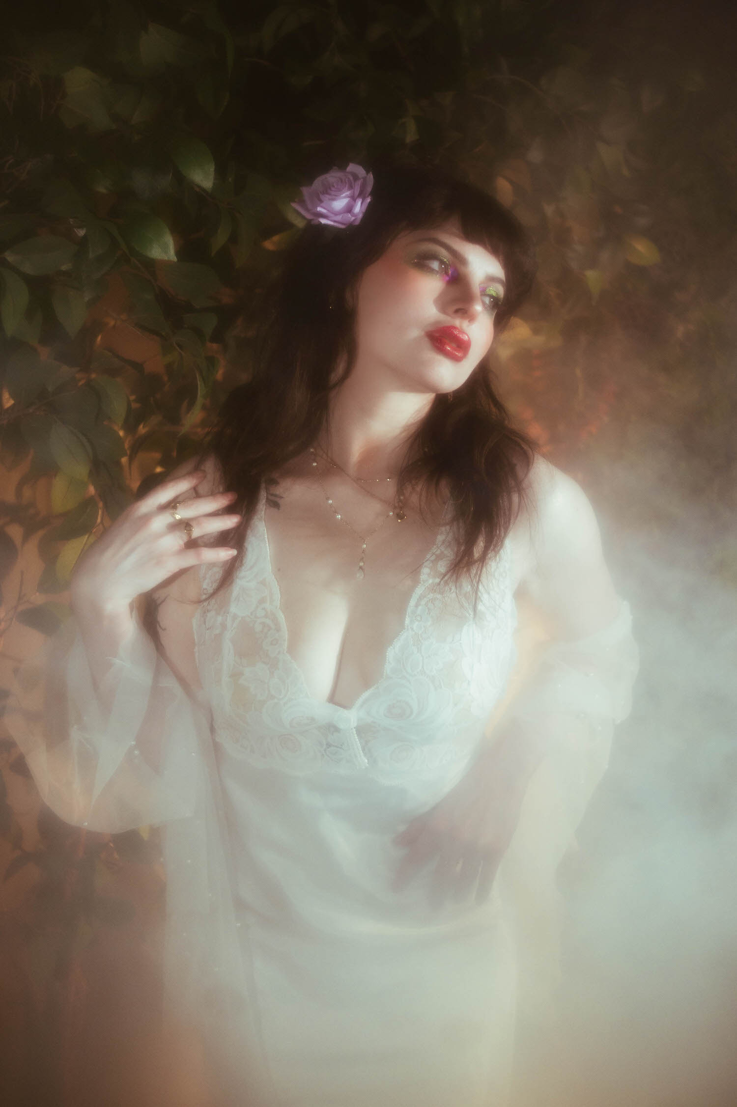 A close up portrait shows a bride with a lilac rose in her hair, bold red lips, and soft fog machine boudoir photography haze glowing warmly behind her inside Royal Lune's vintage photo studio, Royal Lune Photo.