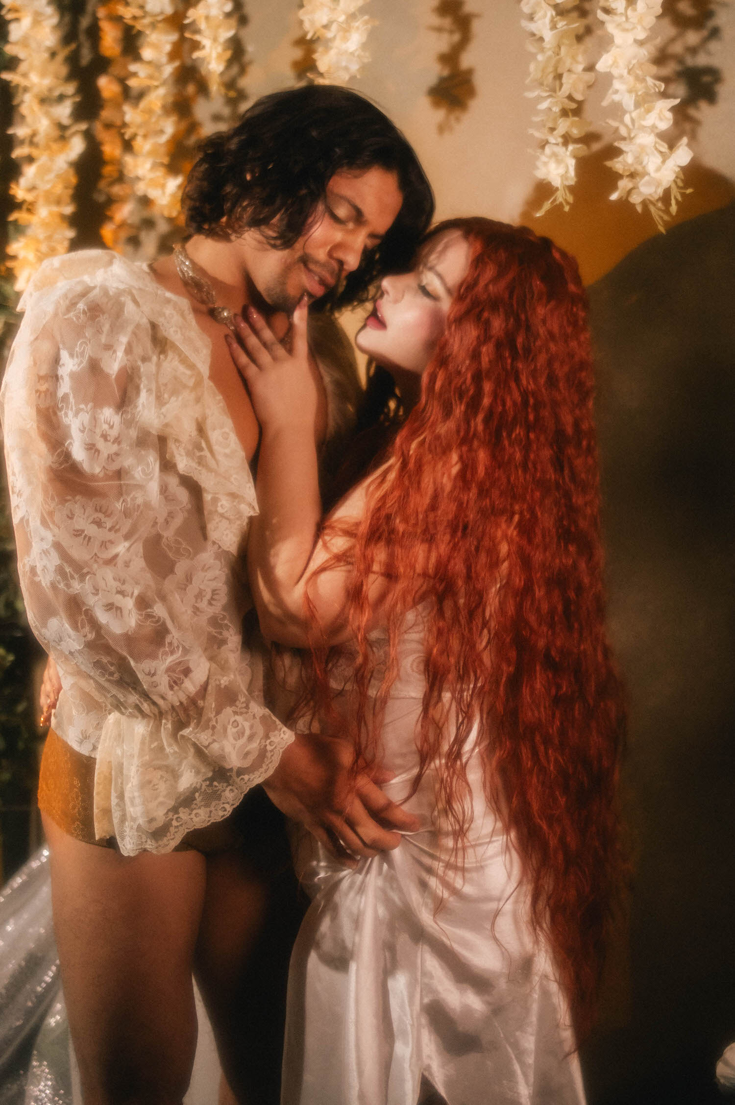 Renaissance boudoir photoshoot detail of a couple face to face, the woman's hand resting against her partner's chest as her red hair cascades past white lace sleeves. Royal Lune Photo