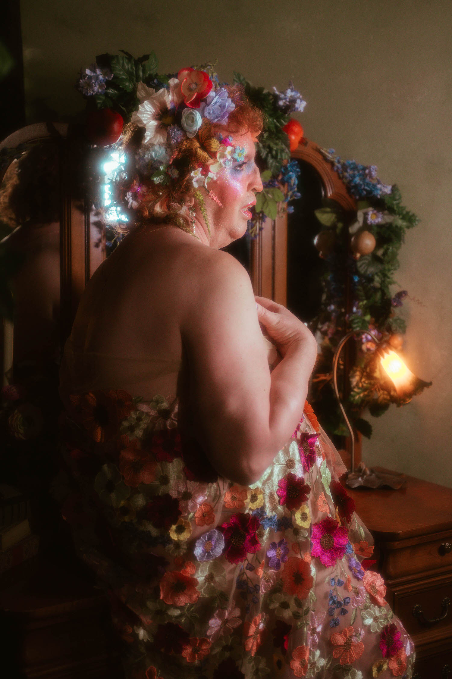 A profile view from this self expression through art session shows a woman's shoulder and flower crown lit by a warm lamp, her floral embroidered gown trailing down her back at Royal Lune Studio. Royal Lune Photo