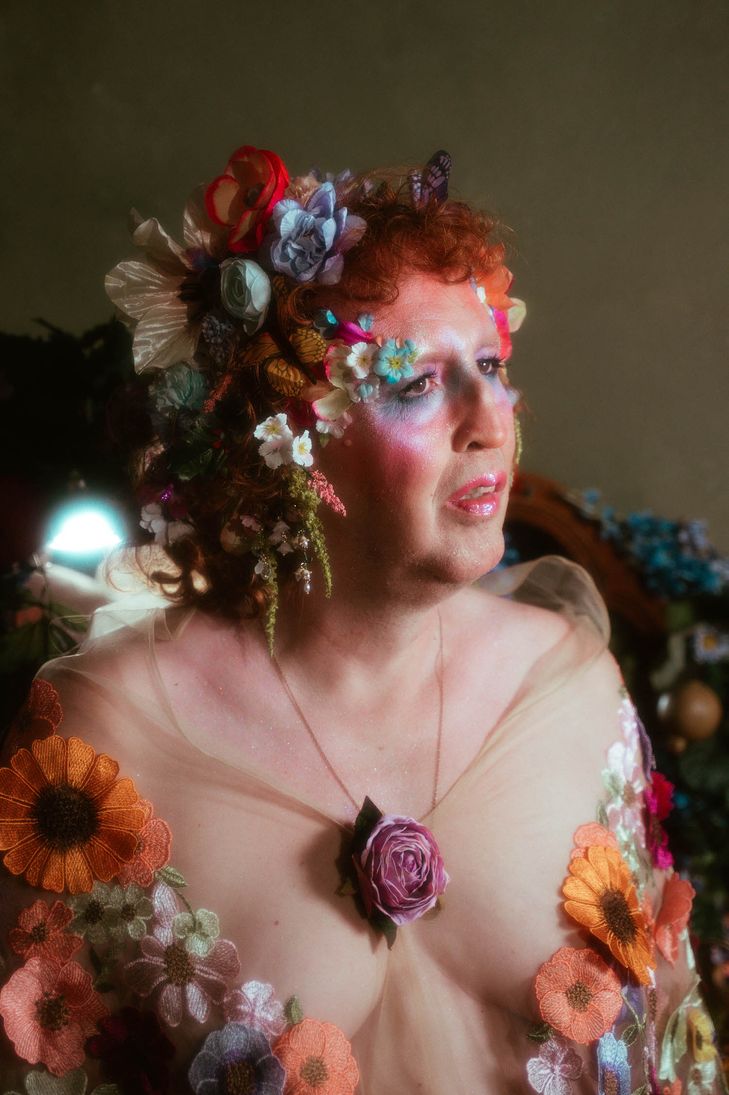 A gender affirming boudoir portrait shows a woman gazing to the side, a rose pendant necklace resting at her chest beneath a flower crown accented with a small butterfly detail. Royal Lune Photo