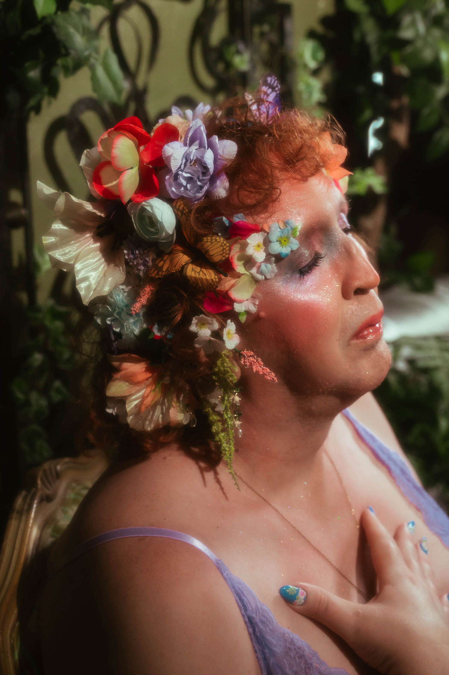 A close up profile from this self expression through art session shows a woman's flower crown of red, lavender, and cream blooms with a monarch butterfly detail, her eyes closed against a backdrop of greenery. Royal Lune Photo