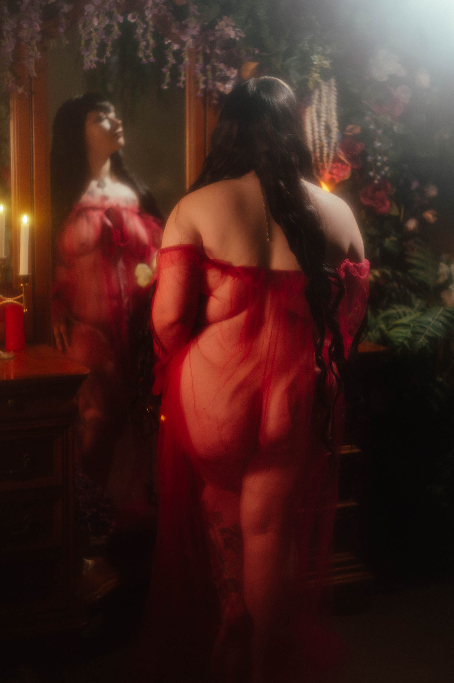 A back view shows a bride in a sheer burgundy duster with her long dark hair down, standing before an antique mirror reflecting florals and candlelight during a gothic bridal boudoir session at Royal Lune Studio, Royal Lune Photo.