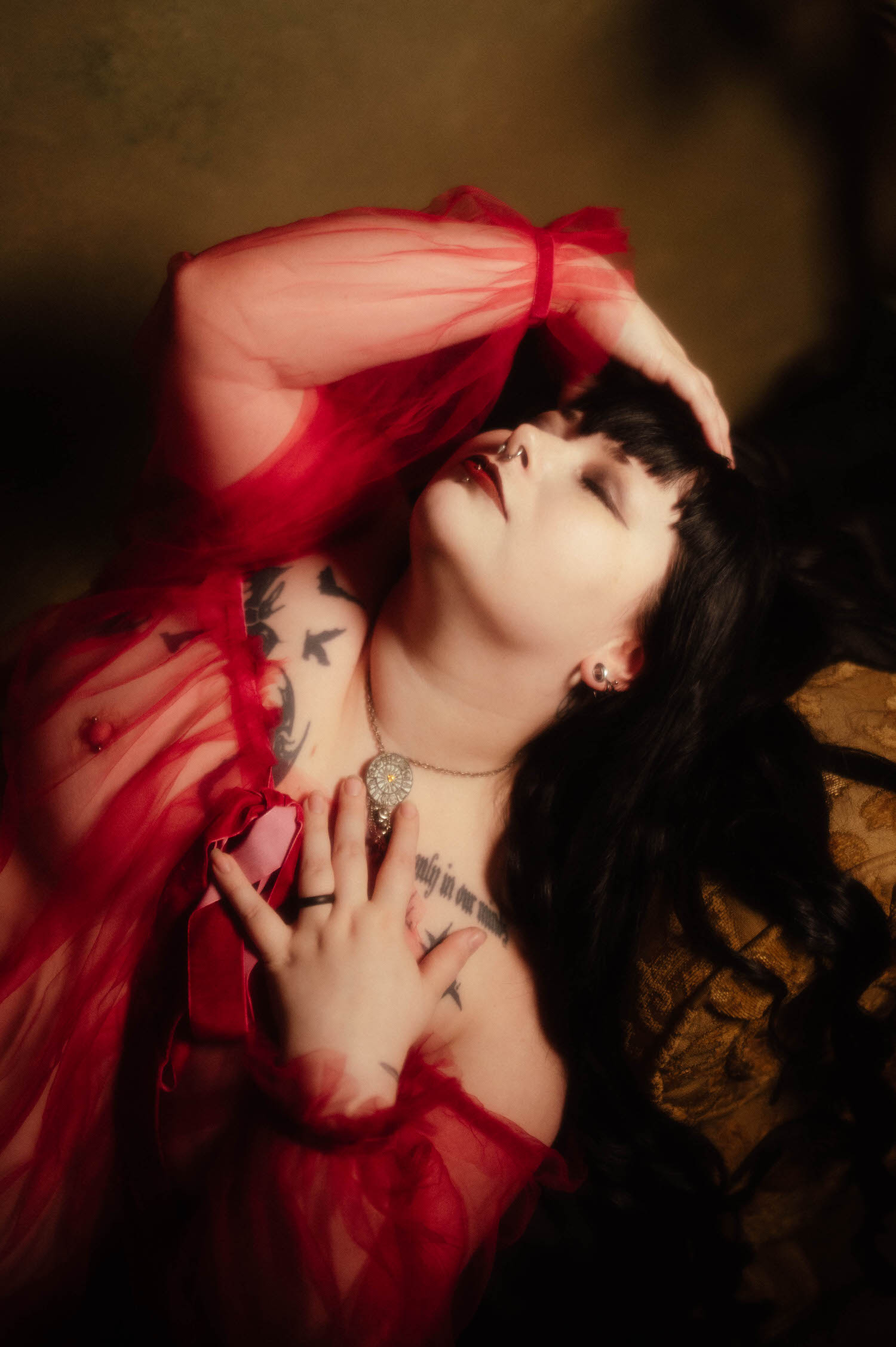 A close up shows a bride with her arm raised overhead in a sheer burgundy duster, her hand resting against her chest tattoos with a ring visible on her finger, photographed at Royal Lune Studio, Royal Lune Photo.