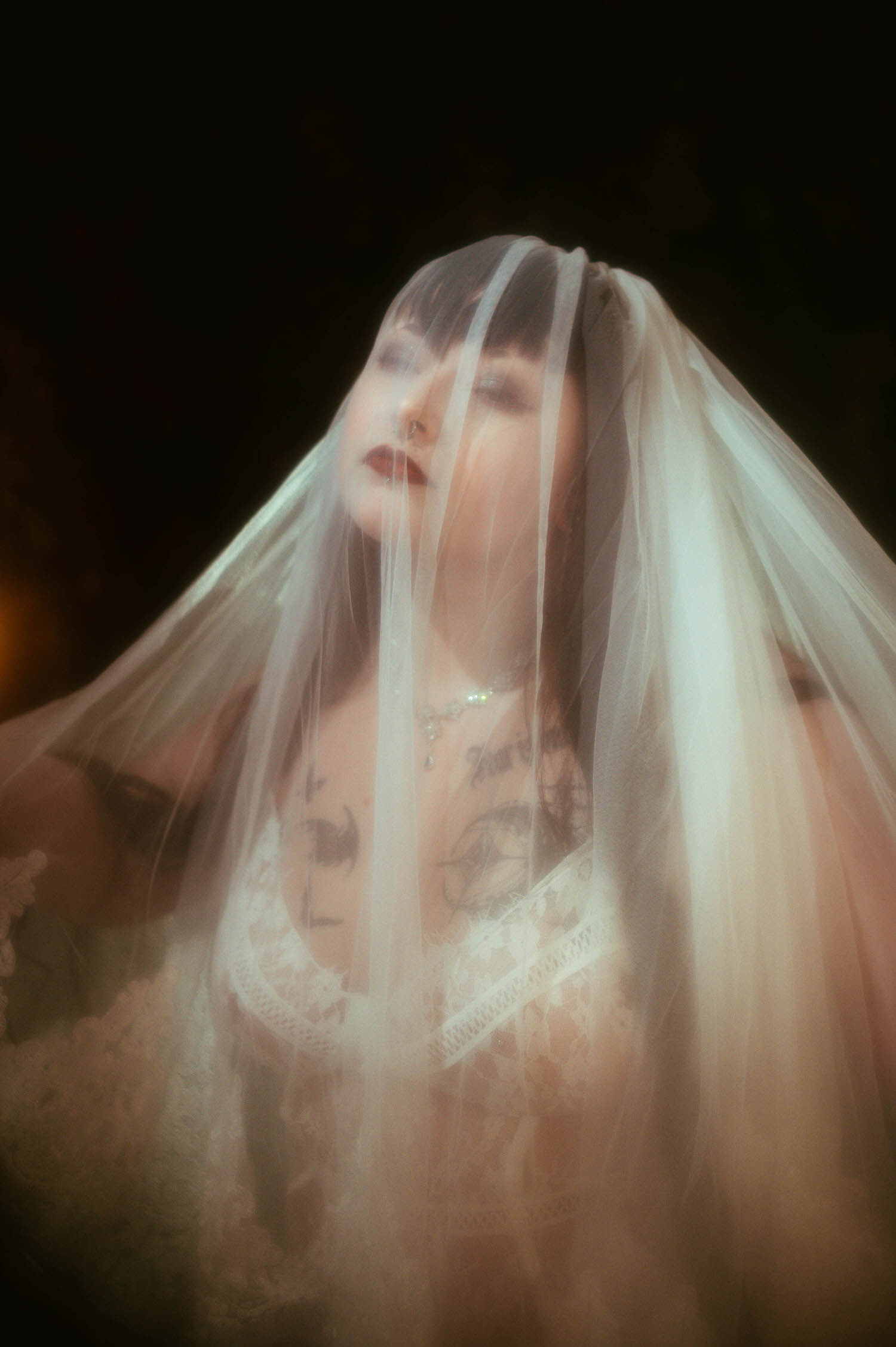 A close up shows a bride with a sheer white cathedral veil pulled forward over her face, revealing a white lace bra beneath, photographed against a dark background at Royal Lune Studio, Royal Lune Photo.