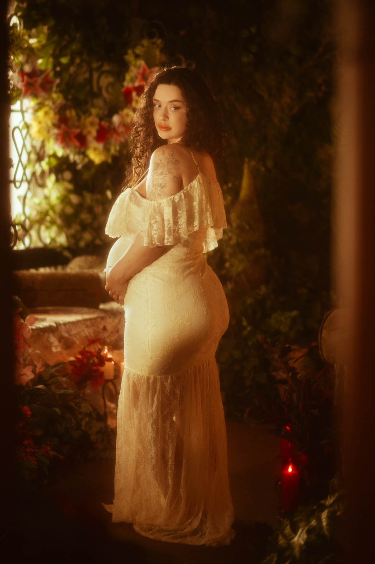 A Dallas maternity photographer captures a mirrored back view of a woman in a fitted ivory lace gown, one hand resting on her belly, showing the gown's mermaid silhouette against a floral backdrop at Royal Lune Photo.