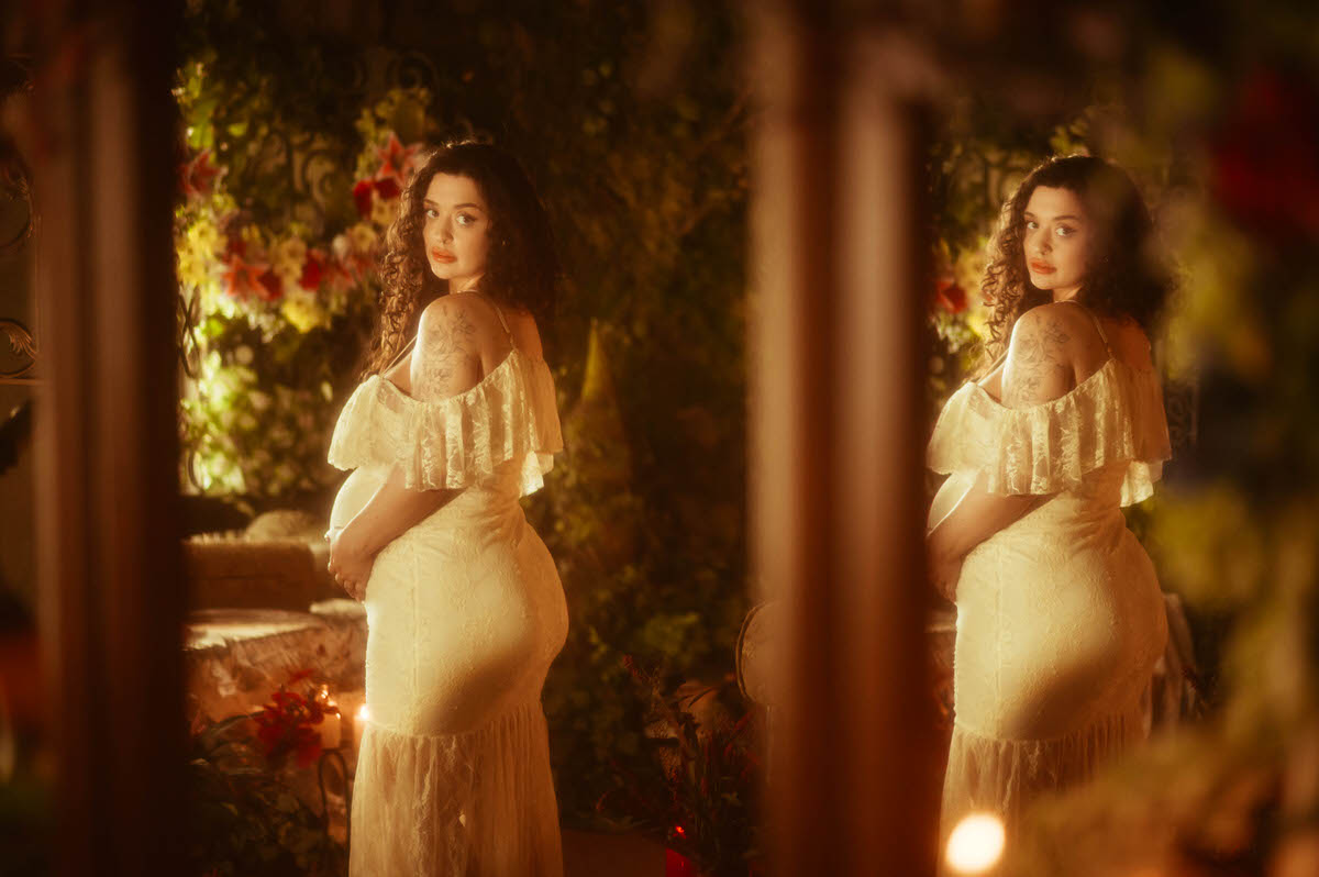 This pregnancy photoshoot idea captures a woman's reflection in an antique mirror, standing in an ivory lace gown with one hand on her belly, floral shoulder tattoo work visible, glancing back over her shoulder at Royal Lune Photo.