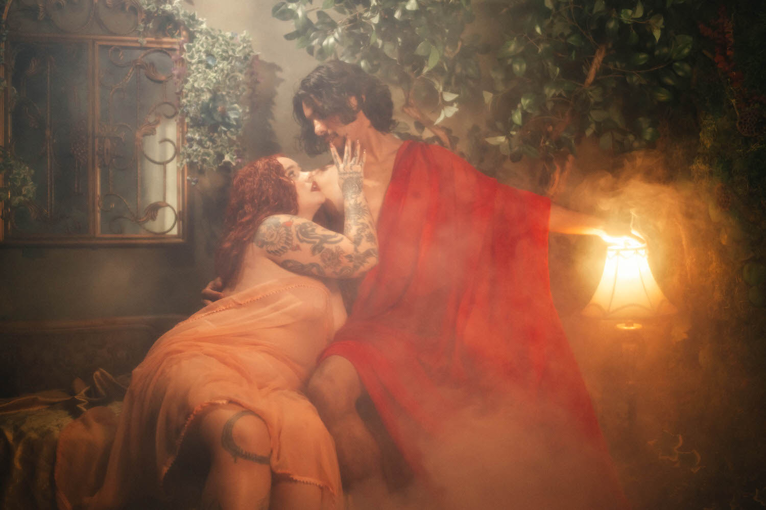 Fine art couples boudoir portrait shows the pair reaching toward a glowing lantern together, wet silk fabric draping over both figures in warm amber tones. Royal Lune Photo