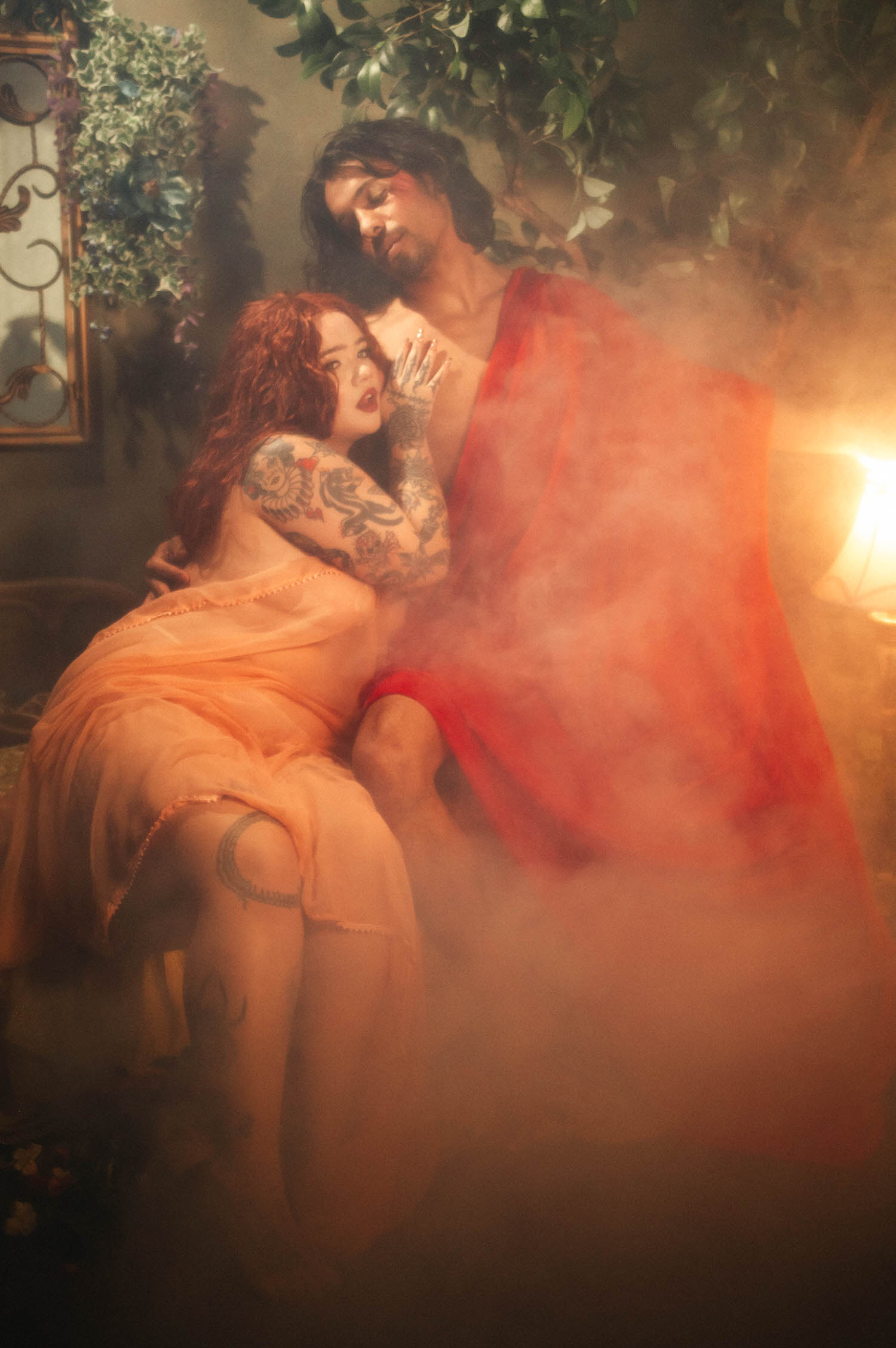 Renaissance inspired photoshoot detail shot of a couple nose to nose, the woman's tattooed arm resting against her partner's chest as sheer smoke curls behind them. Royal Lune Photo