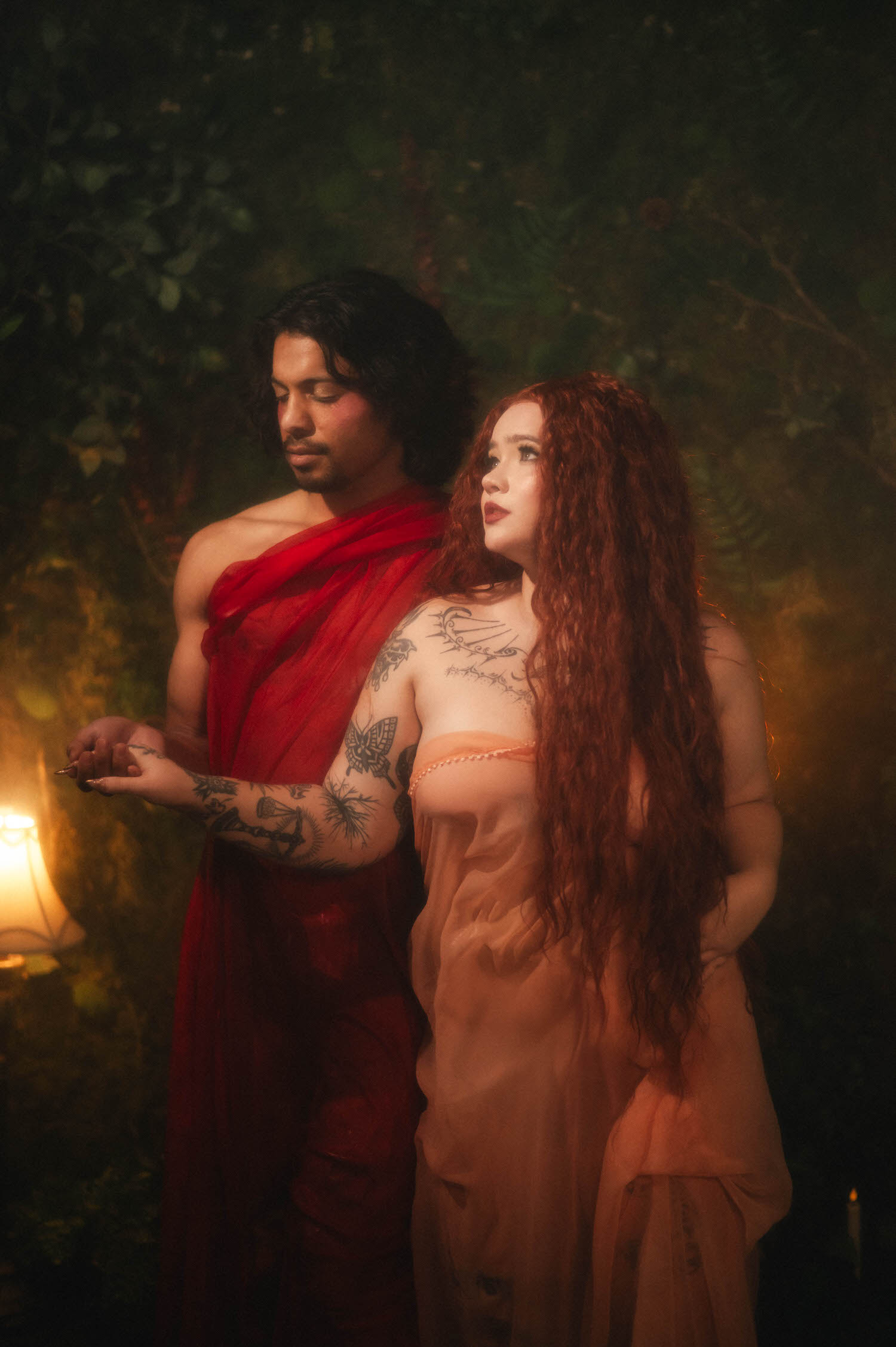 A statue inspired photoshoot detail shows the couple standing side by side in wet draped fabric, the man's tattooed hand catching soft firelight. Royal Lune Photo
