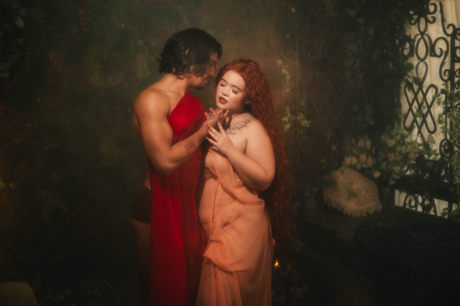 Couples boudoir photoshoot ideas come to life beside a wrought iron gate, the pair standing close as the woman's hand rests against her chest. Royal Lune Photo