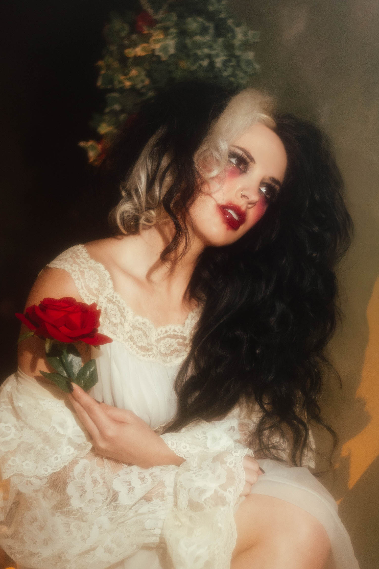A close up portrait shows a model in an ivory lace dress with a red rose resting on her shoulder and dramatic red lipstick in this Taylor Swift album inspired photoshoot by Royal Lune Photo.