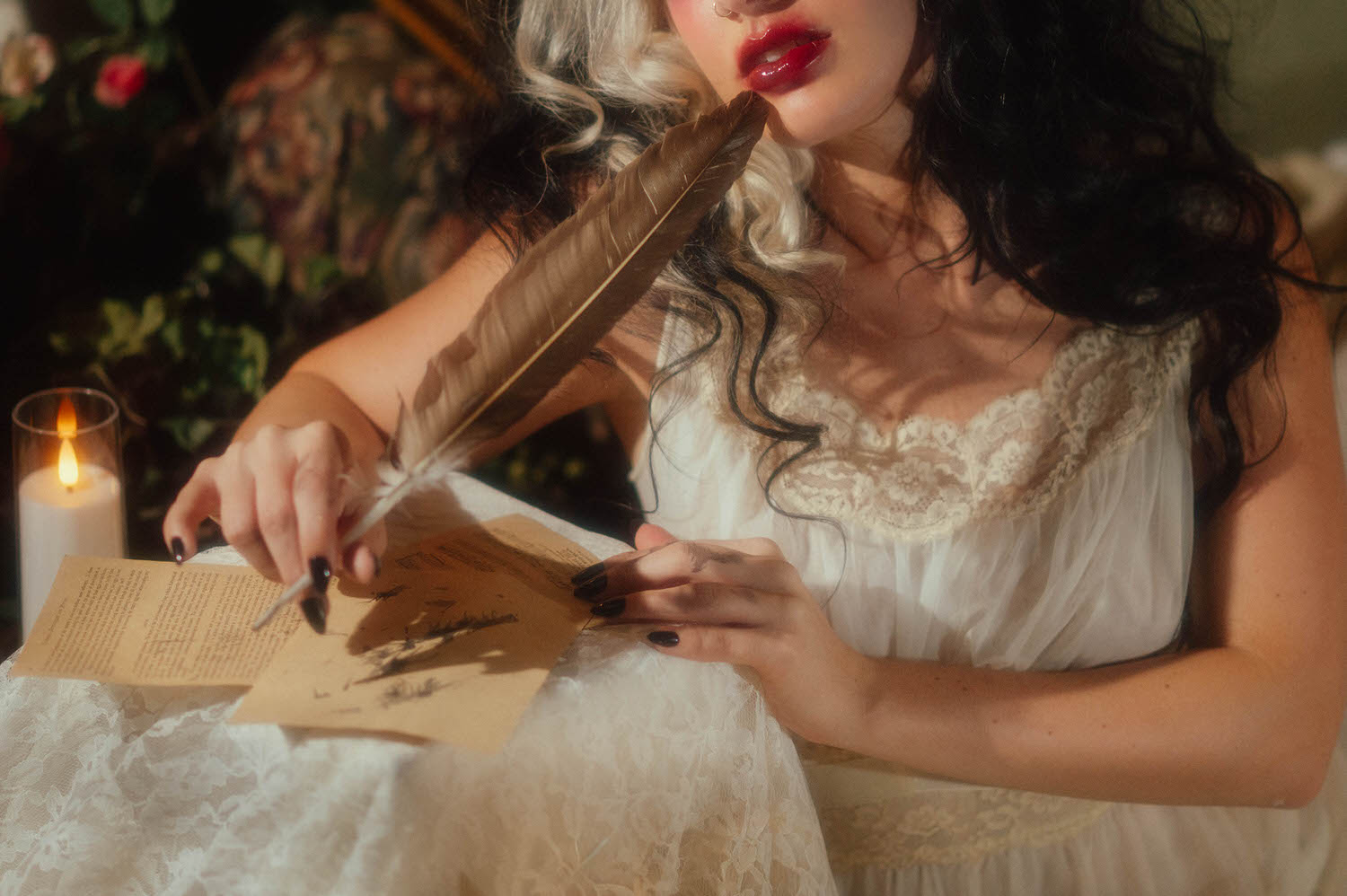 A close up image shows a model's hands with dark polished nails holding a quill pen over handwritten letters beside a lit candle in this Taylor Swift album inspired photoshoot by Royal Lune Photo.