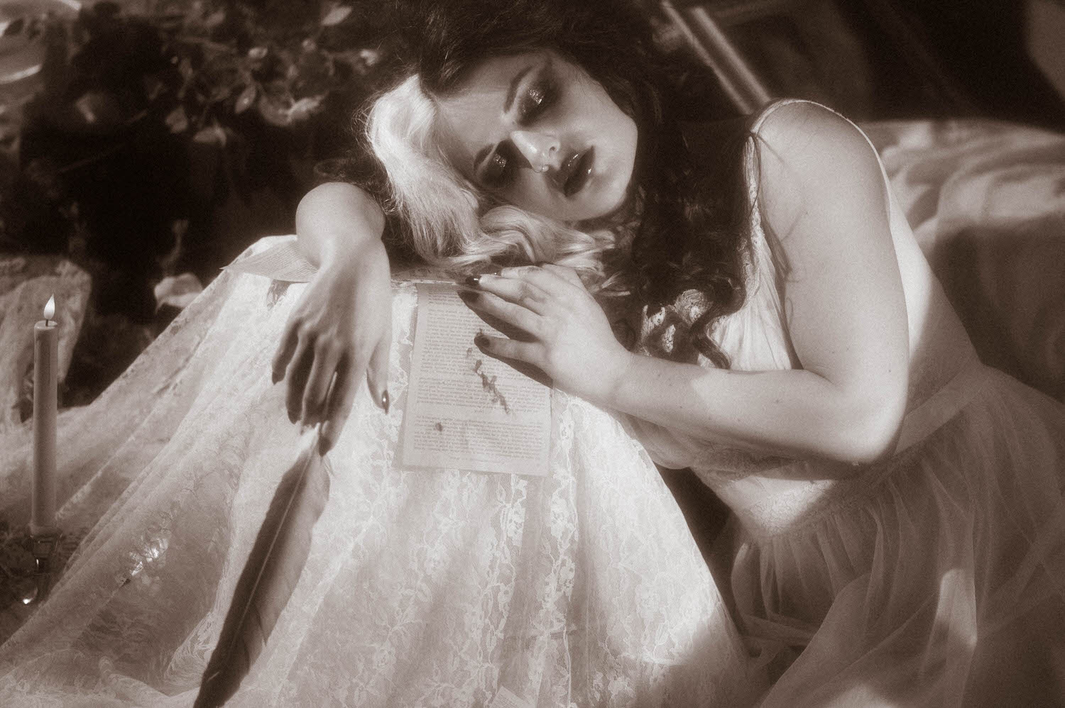 A black and white portrait shows a model reclining with a handwritten letter resting on her lace skirt beside a lit candle in this moody poetry photoshoot by Royal Lune Photo.