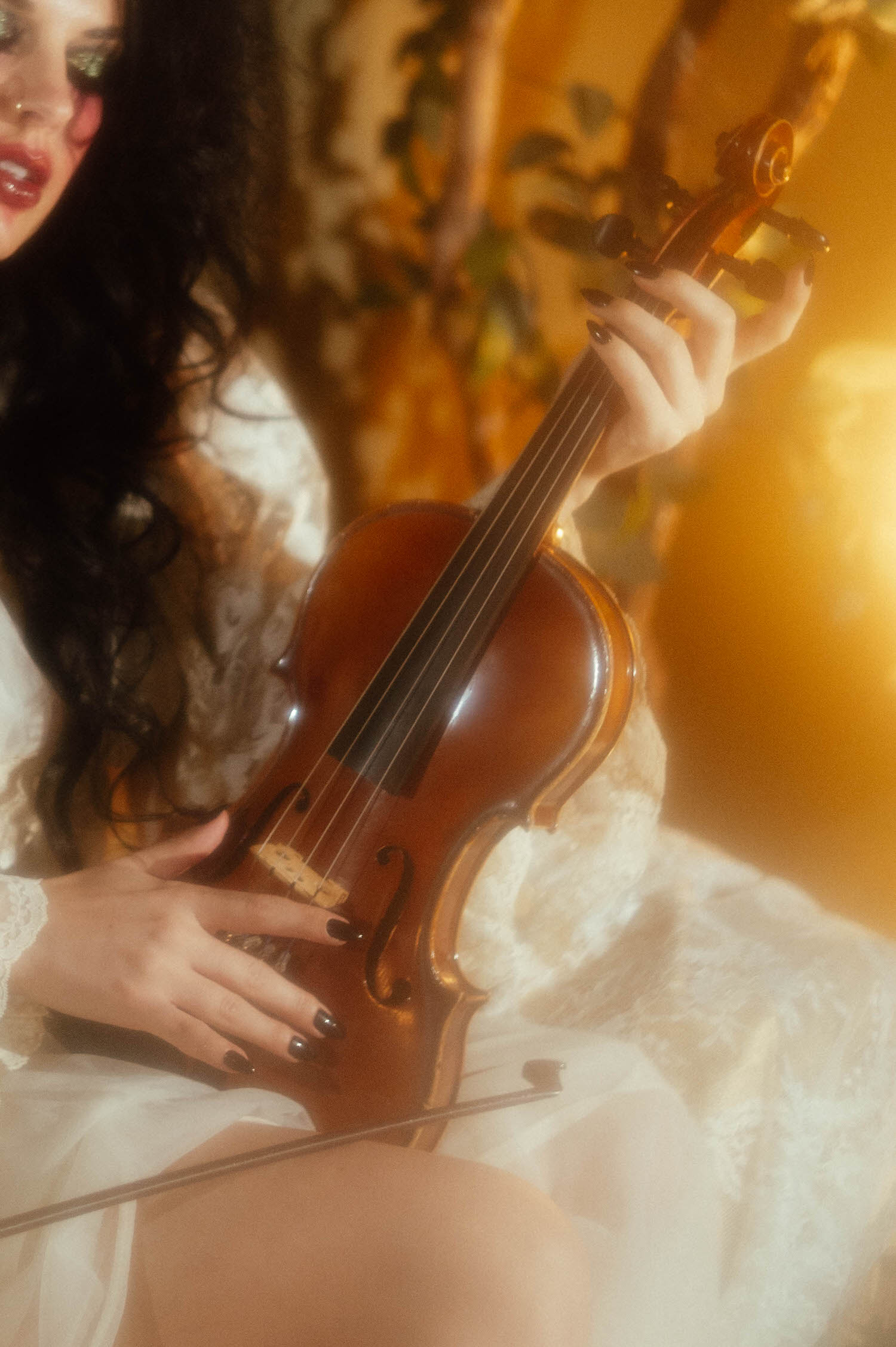 A close up image shows a model's hands with dark polished nails resting on the body of a violin in soft golden light during this Tortured Poets Department photoshoot by Royal Lune Photo.