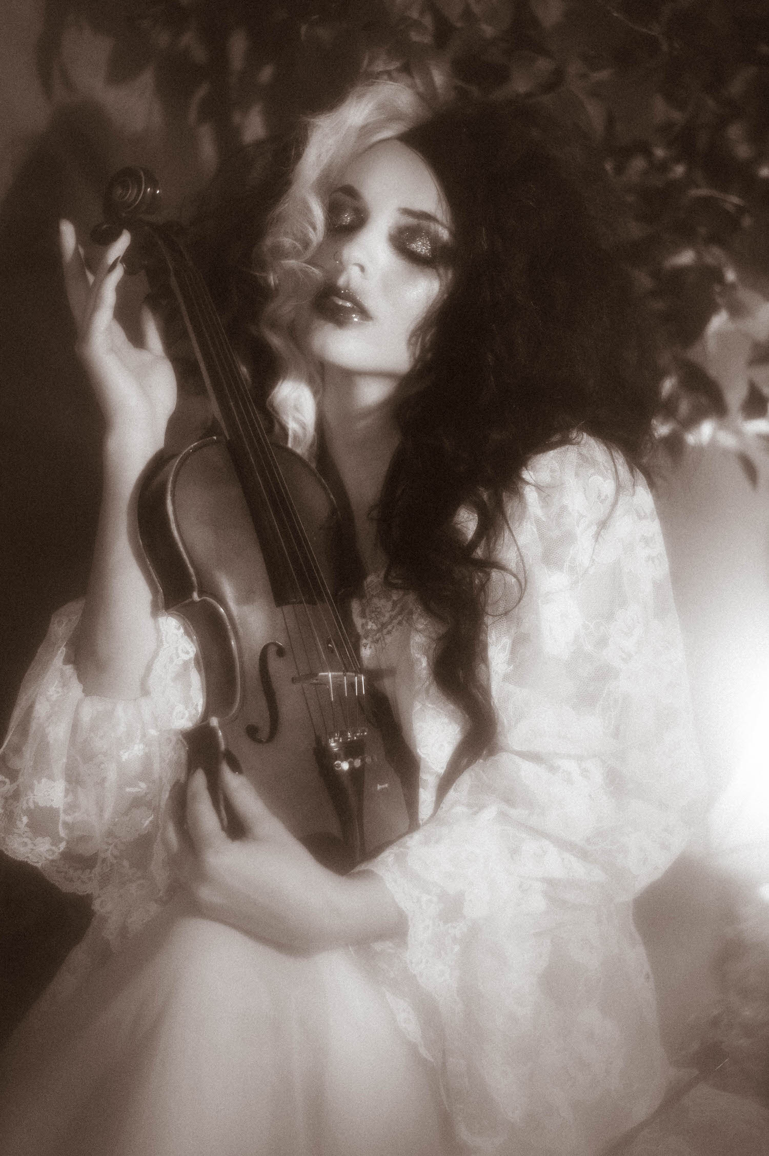 A black and white close up portrait captures a model with dark curls and glittering eye makeup holding a violin close to her chest in this moody poetry photoshoot by Royal Lune Photo.