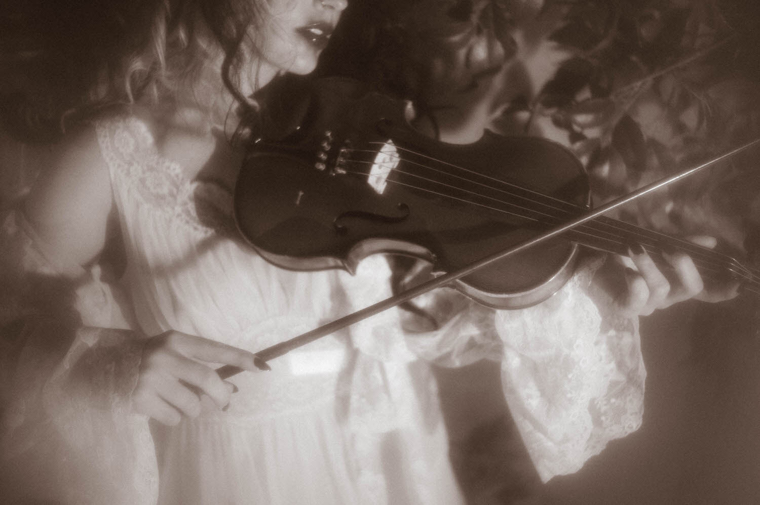 A black and white close up image shows a model's hands drawing a bow across violin strings while wearing an ivory lace sleeve in this Tortured Poets Department photoshoot by Royal Lune Photo.