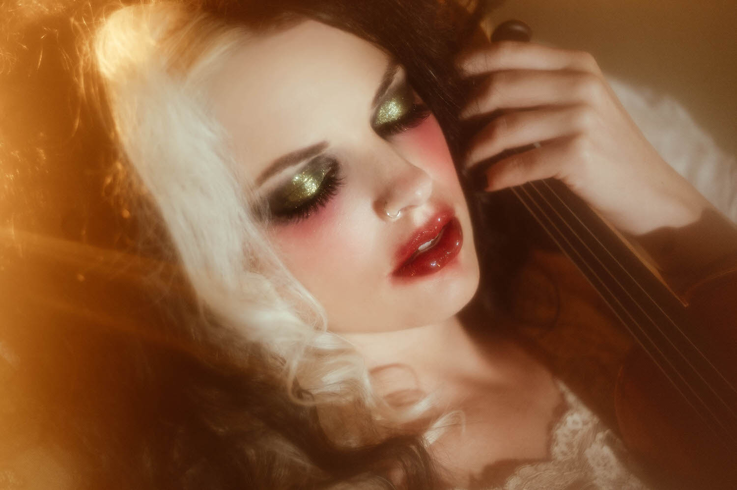 A close up portrait shows a model's glittering green eyeshadow and smudged red lips resting against a violin in warm golden light in this moody poetry photoshoot by Royal Lune Photo.