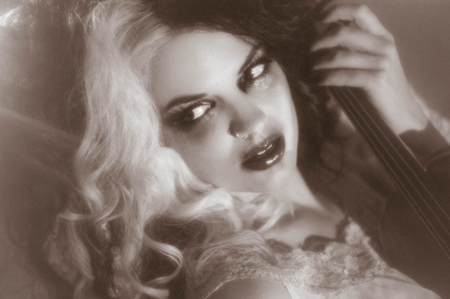 A black and white close up captures a model's tear streaked eyes and dark lips while holding a violin neck in this Tortured Poets Department photoshoot by Royal Lune Photo.