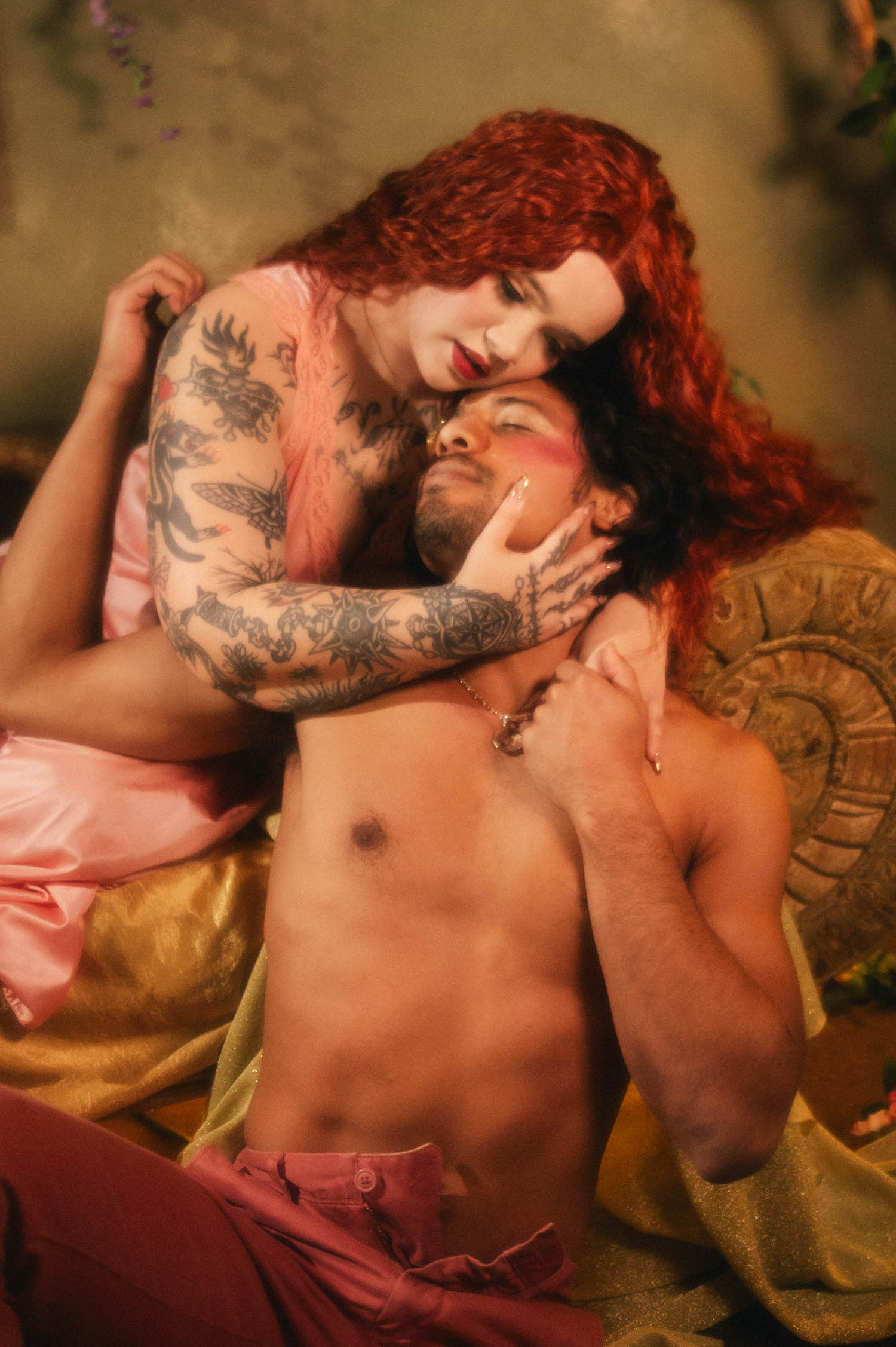 A couples boudoir photoshoot idea captured mid embrace, the woman's tattooed hand resting against her partner's jaw as they rest together against a carved wooden armrest. Royal Lune Photo