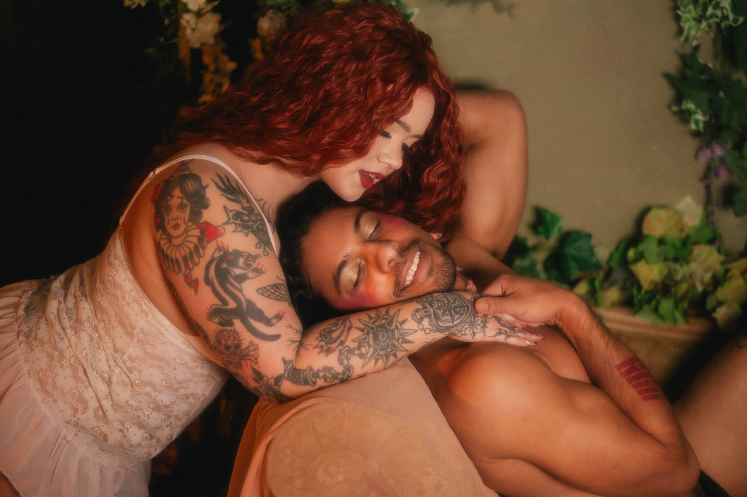Close up portrait from a queer couples boudoir session showing two faces nearly touching, white lace straps and bold tattoo work contrasted against soft golden light. Royal Lune Photo