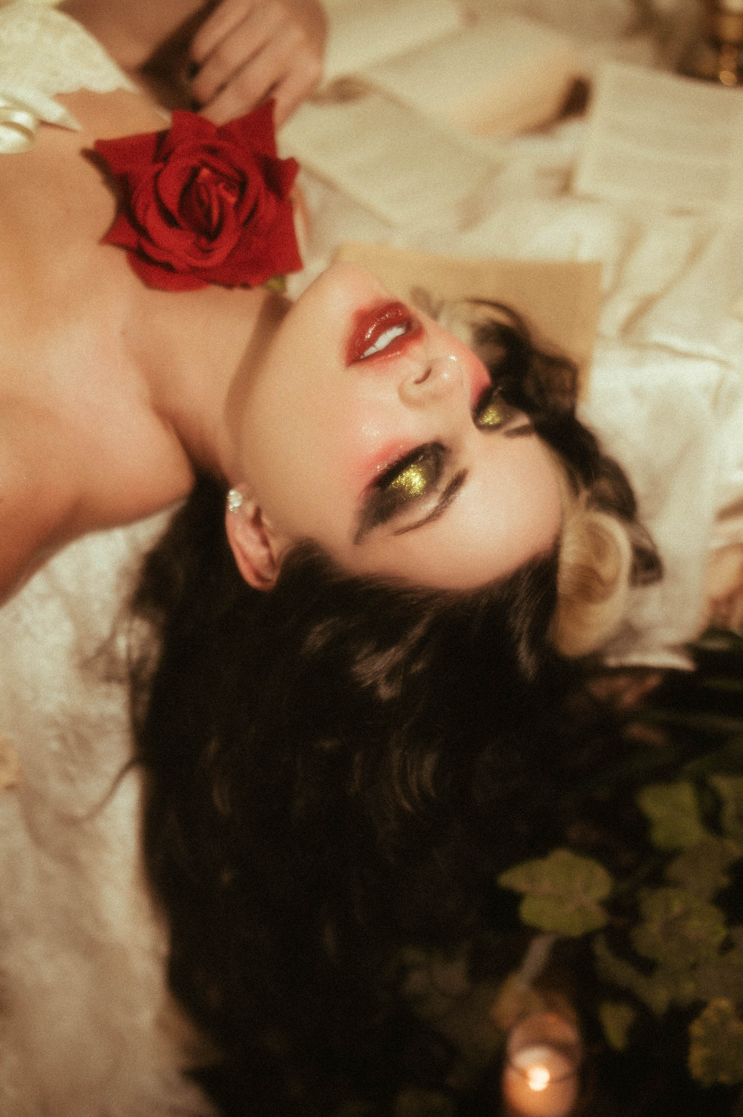 A close up portrait highlights a model's glittering gold and green eye makeup and bold red lips beside a red rose in this heartbreak photoshoot idea captured by Royal Lune Photo.