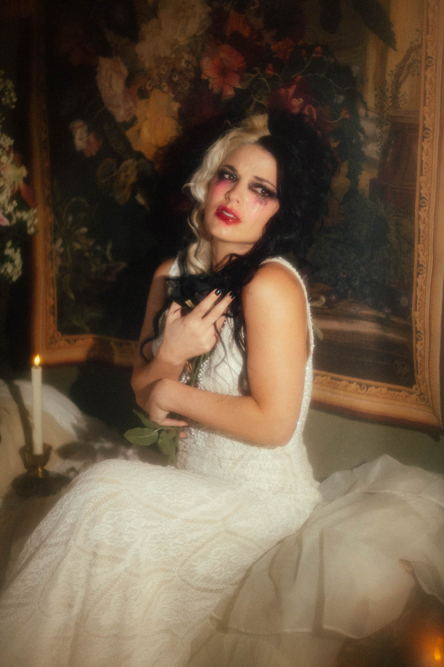 A model in a lace wedding gown holds a black rose against her chest with smudged tears streaking her makeup in this heartbreak photoshoot idea by Royal Lune Photo.