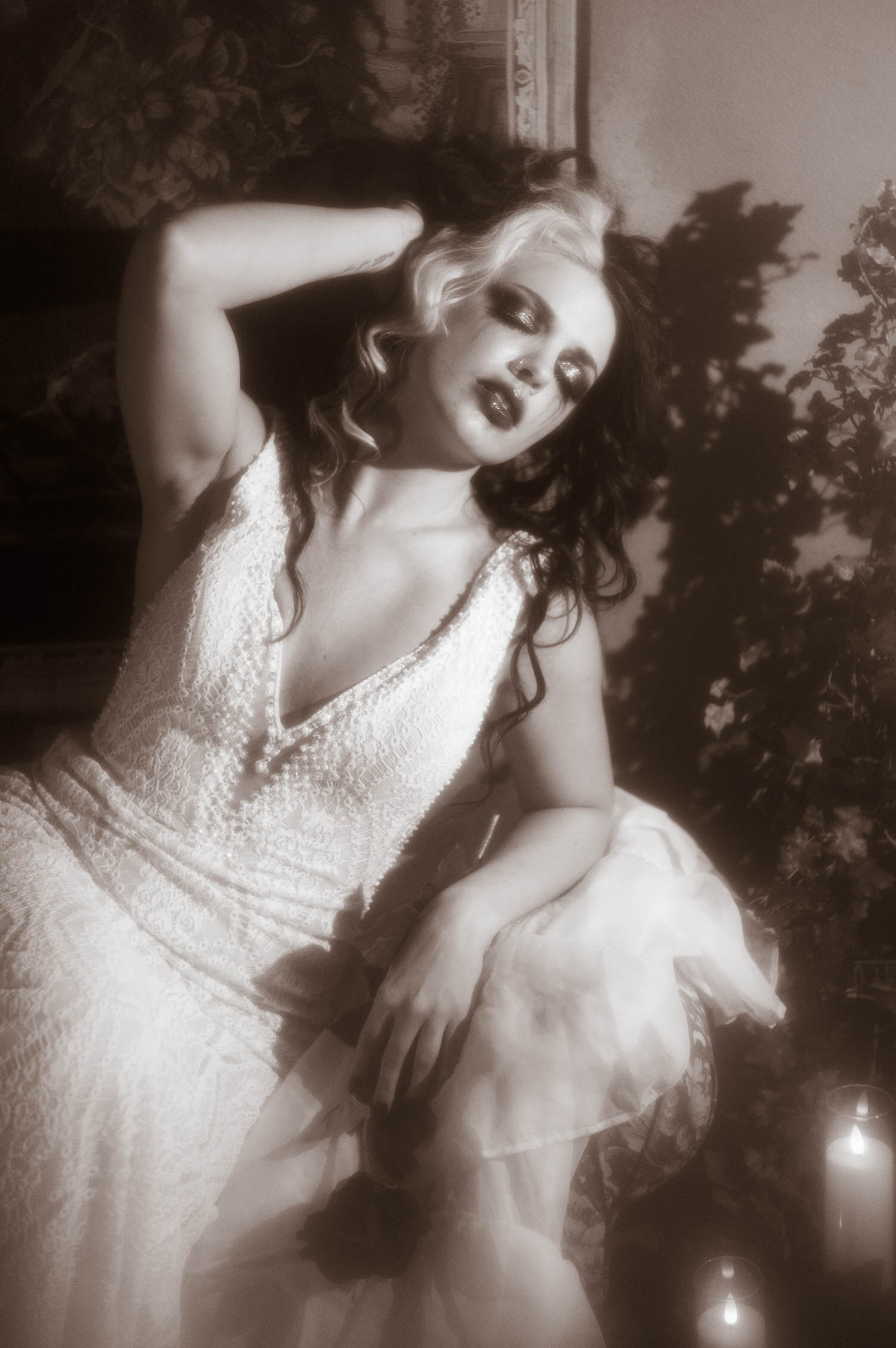  A black and white portrait shows a model in a lace wedding gown seated with one arm resting behind her head in this gothic boudoir photography session by Royal Lune Photo.