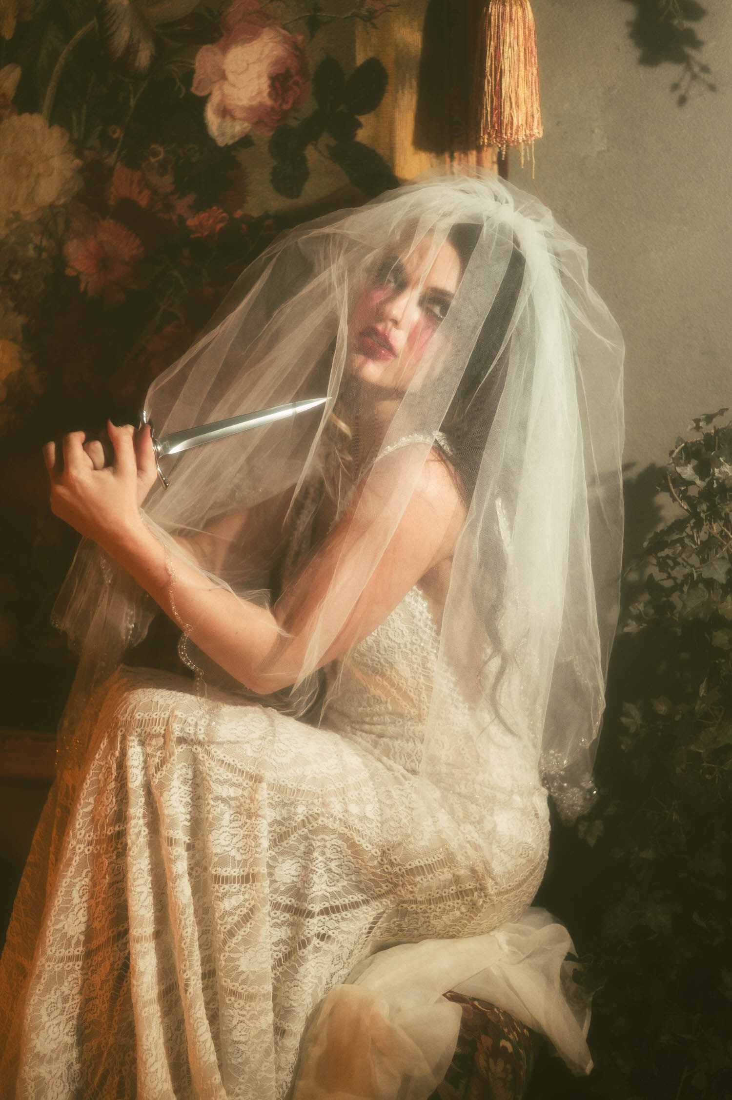A close up portrait shows a model beneath a sheer veil holding a dagger near her smudged makeup in this heartbreak photoshoot idea by Royal Lune Photo.