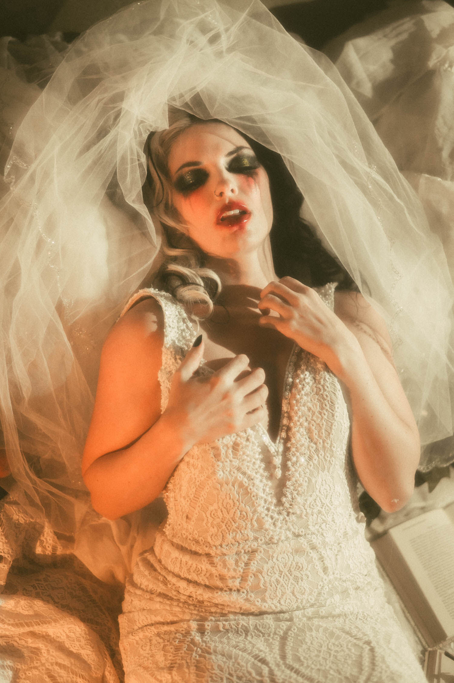 A close up portrait shows a model in a lace wedding gown with her veil lifted, hands clutched at her chest with smudged makeup in this moody poetry photoshoot by Royal Lune Photo.