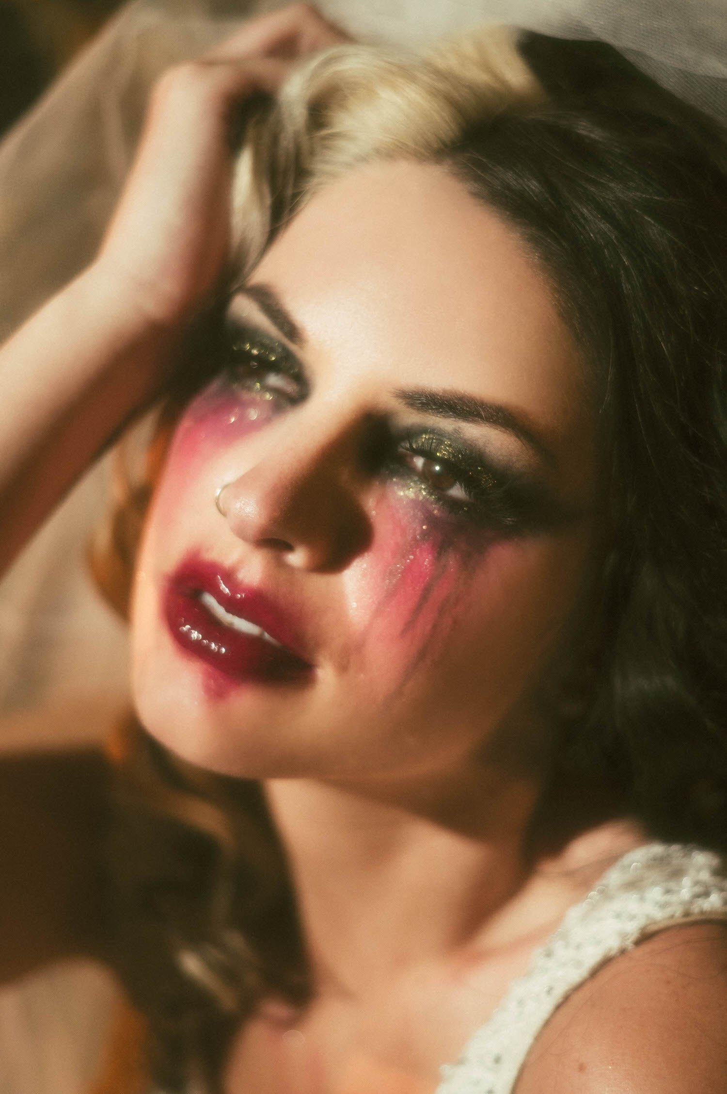 A close up captures a model's tear streaked, smudged editorial gothic style makeup and glossy red lips in this heartbreak inspired photoshoot by Royal Lune Photo.