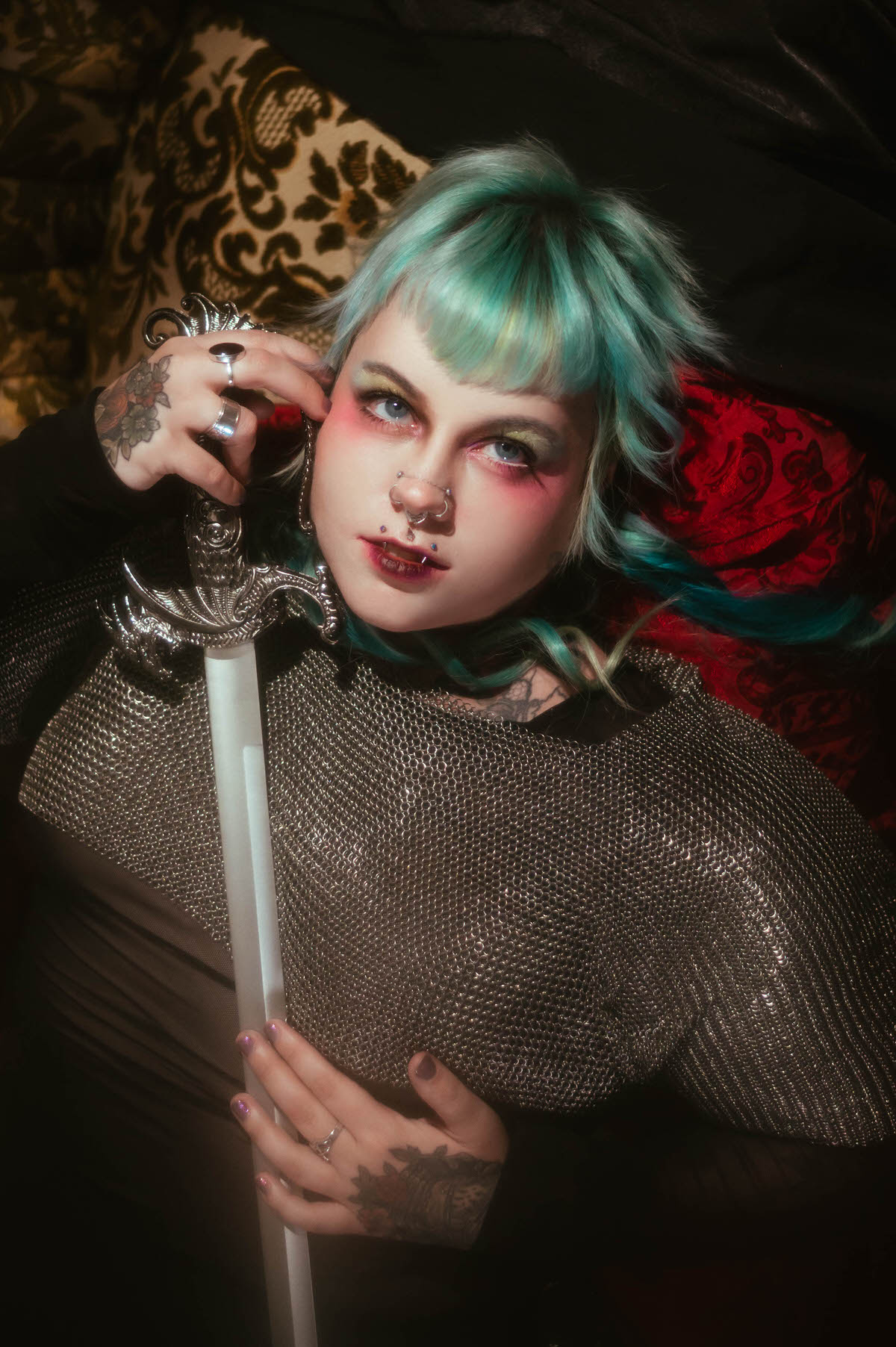 A Dallas Fort Worth branding photographer overhead image of a woman reclining with a sword held across her chainmail top, a crystal star ornament resting on dark fabric nearby, Royal Lune Photo.