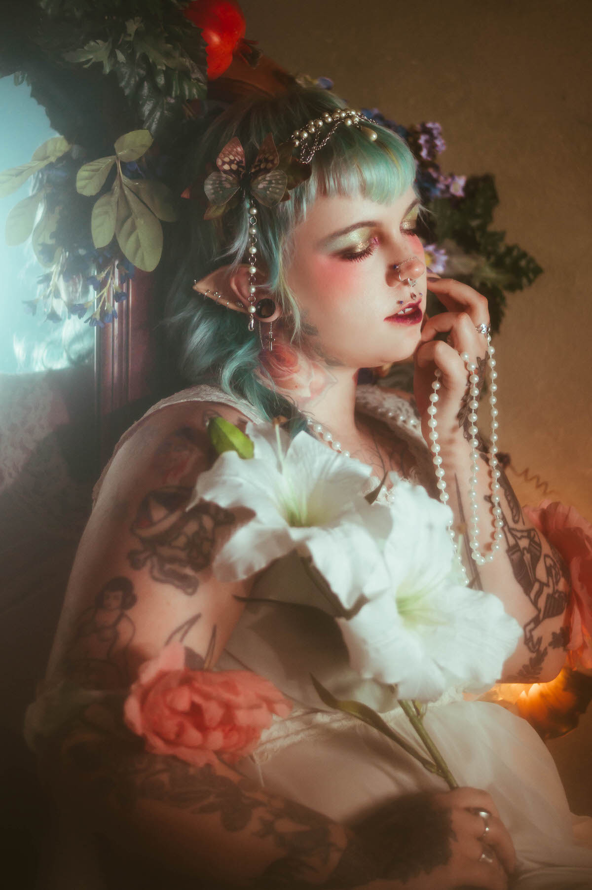 A close up tattoo artist branding photography image of a woman holding white lily and pink peony flowers close to her chest, eyes closed, wearing a pearl and butterfly hair clip with soft gold shimmer eye makeup, Royal Lune Photo.