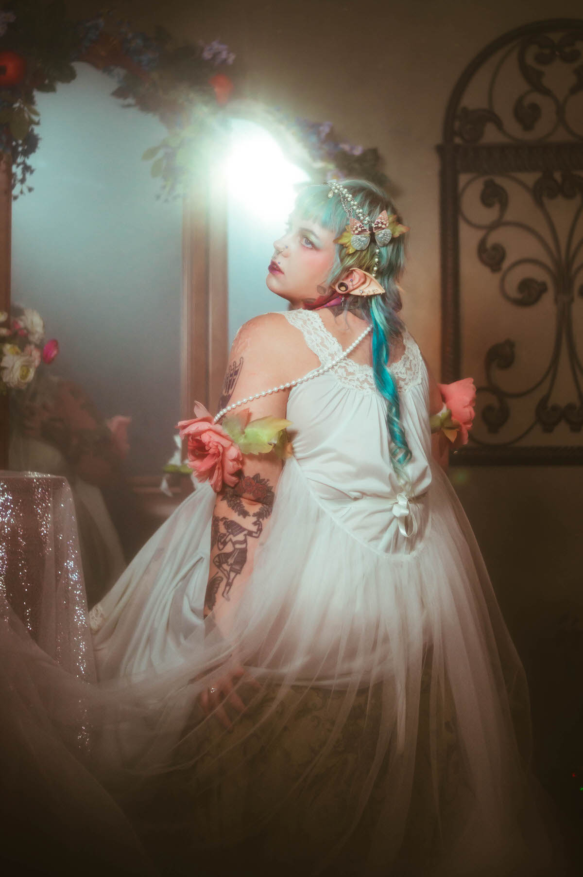 A fantasy branding photoshoot side profile image of a woman looking upward with a pink peony tucked at her shoulder, her tattooed arm visible as her pale dress catches bright backlighting, Royal Lune Photo.