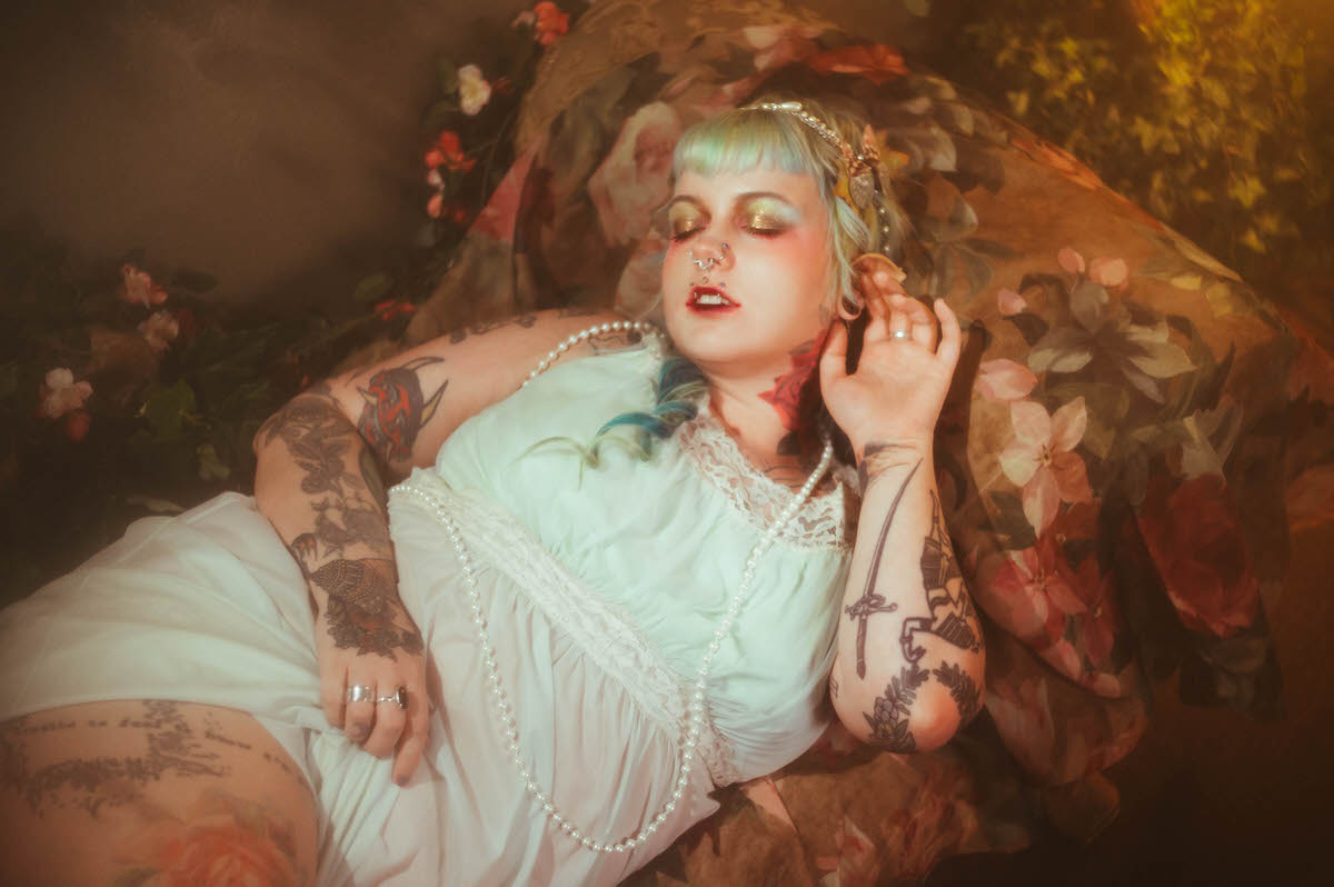 A content photography for creatives in Dallas image of a woman reclining in a mint green nightgown with pearls draped across her chest, eyes closed with soft pink and gold makeup among floral fabric, Royal Lune Photo.