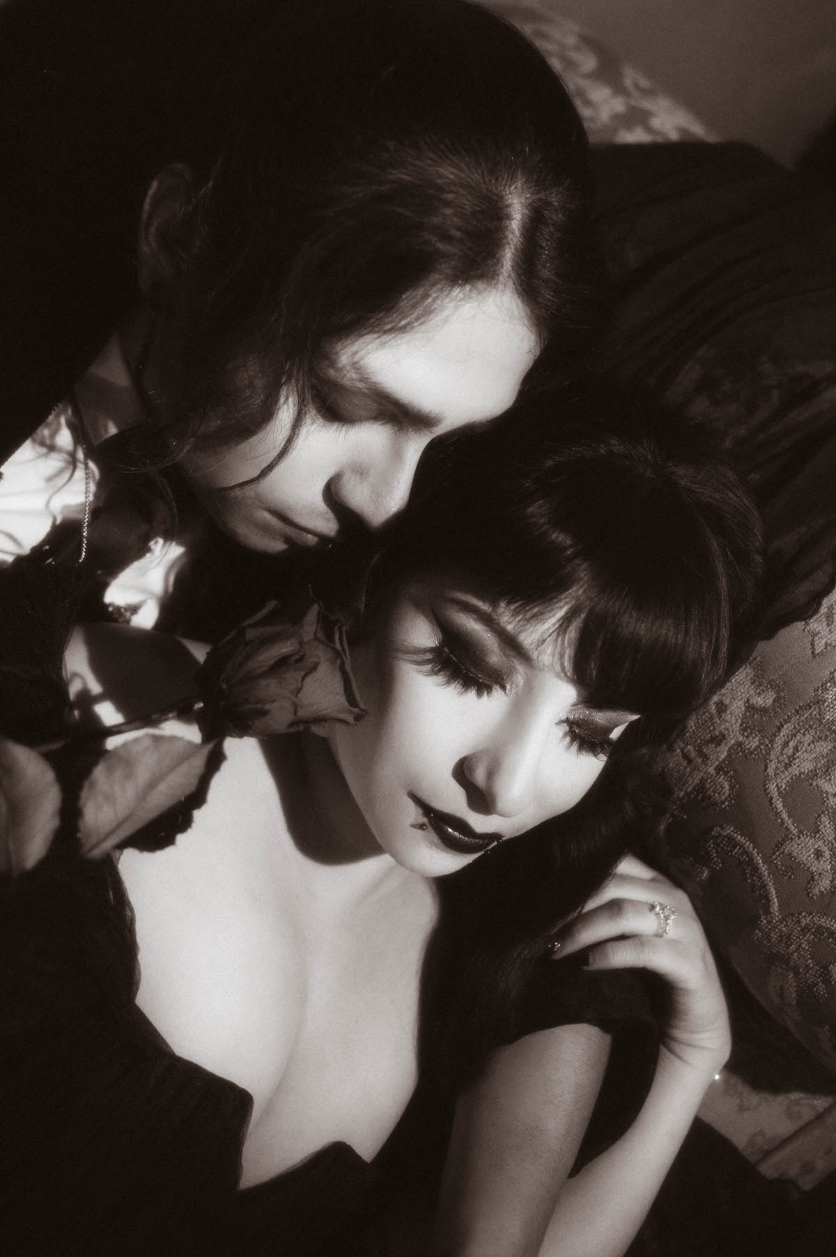 Black and white close-up of a couple nuzzling with a rose between them for dark romantic engagement photography