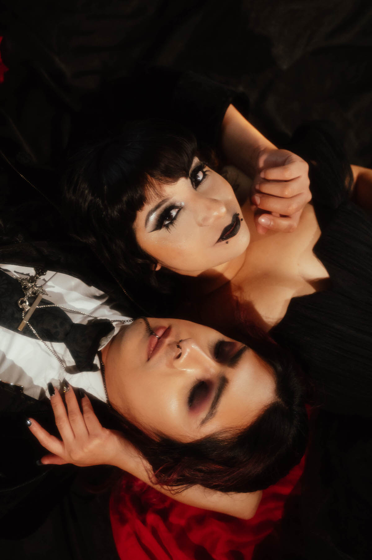Overhead close-up of a couple lying together in dramatic eye makeup and black lipstick for gothic bride and groom photos