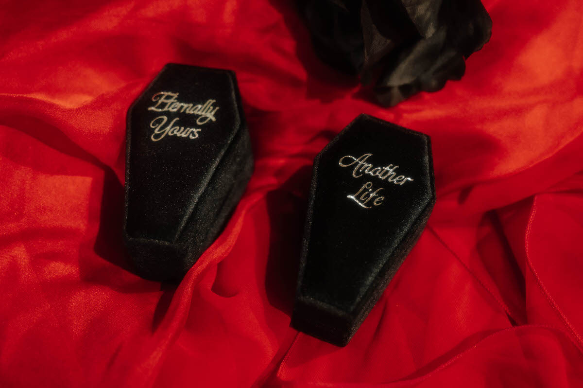 Black velvet coffin ring boxes engraved Eternally Yours and Another Life on red fabric for dark fantasy engagement photos