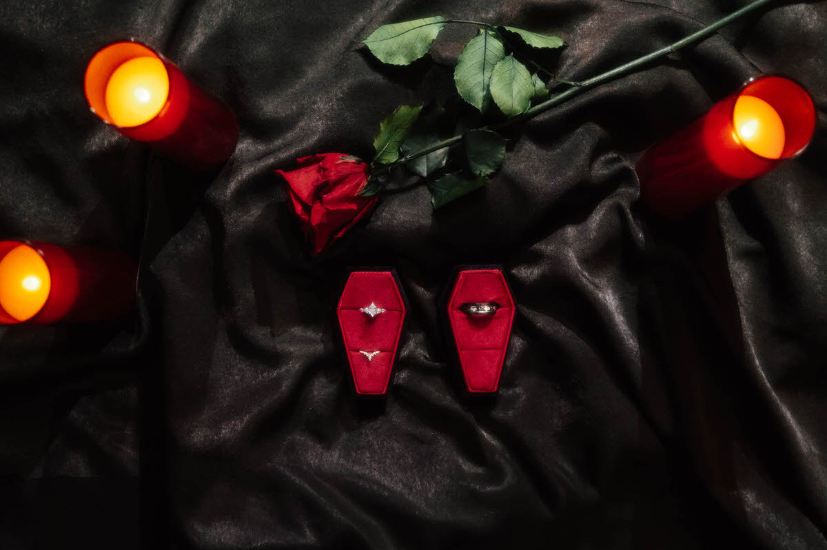Wedding rings in coffin-shaped red velvet boxes with red flameless candles and a rose for dark fantasy engagement photos