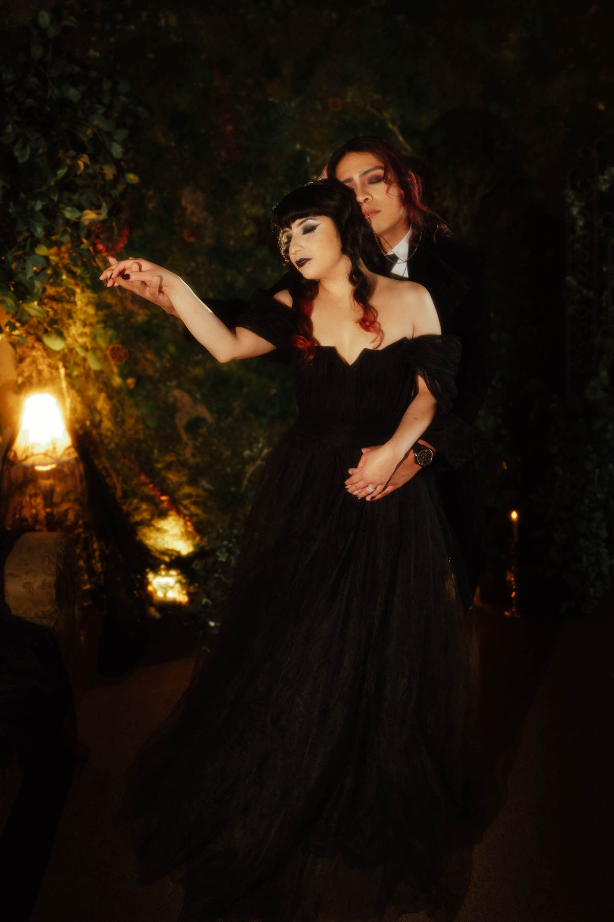 Couple in a black tulle gown and velvet coat posed with one arm outstretched for dark fantasy engagement photos