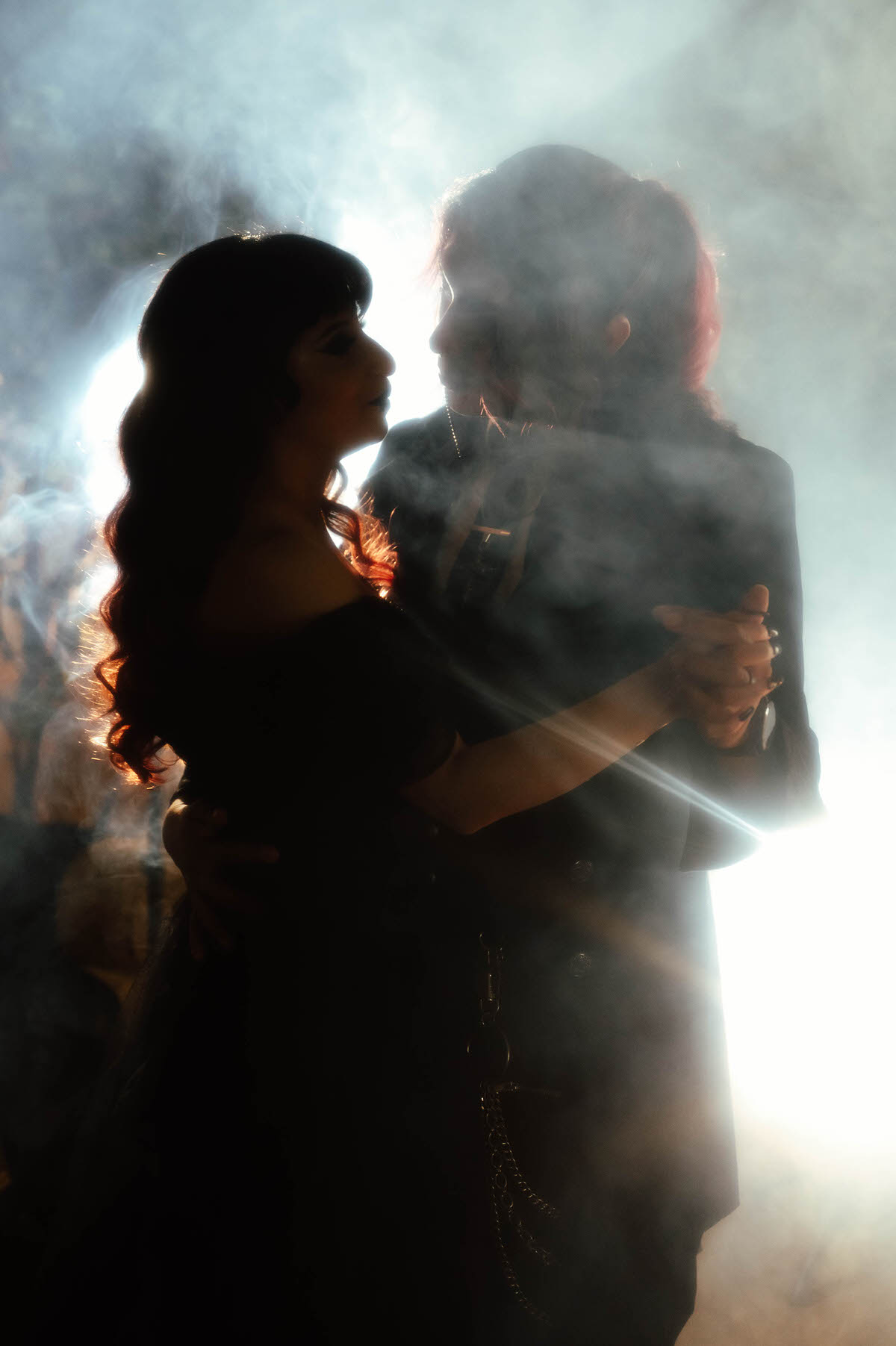 Silhouette of a couple dancing in glowing fog with hands clasped for gothic couples photography