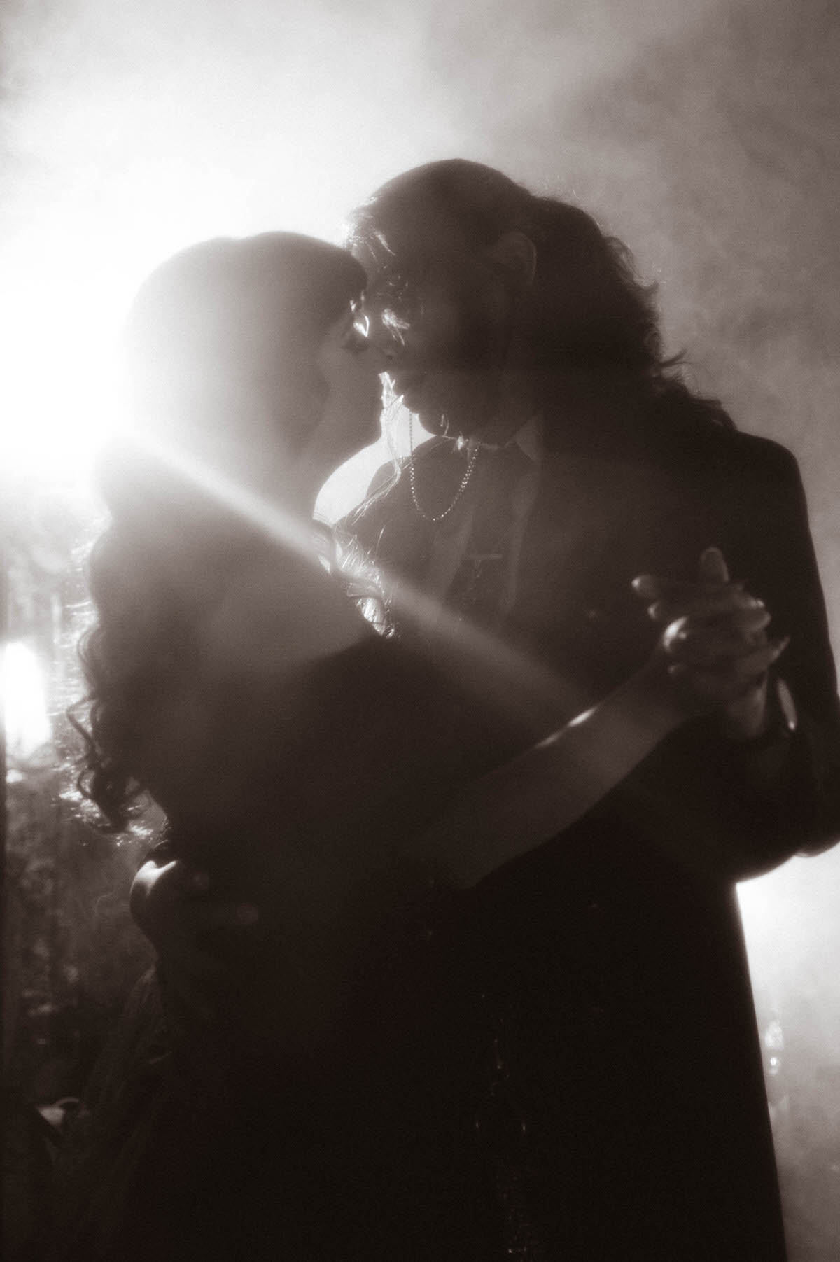 Black and white portrait of a couple dancing close together in backlit fog for a mood engagement session in Dallas